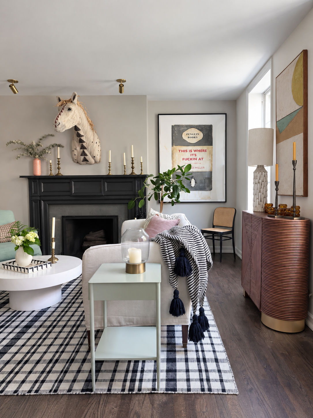 Livingroom with black mantel, large horse head sculpture, black and white checkered rug, linen sofa and a large painting of a book cover