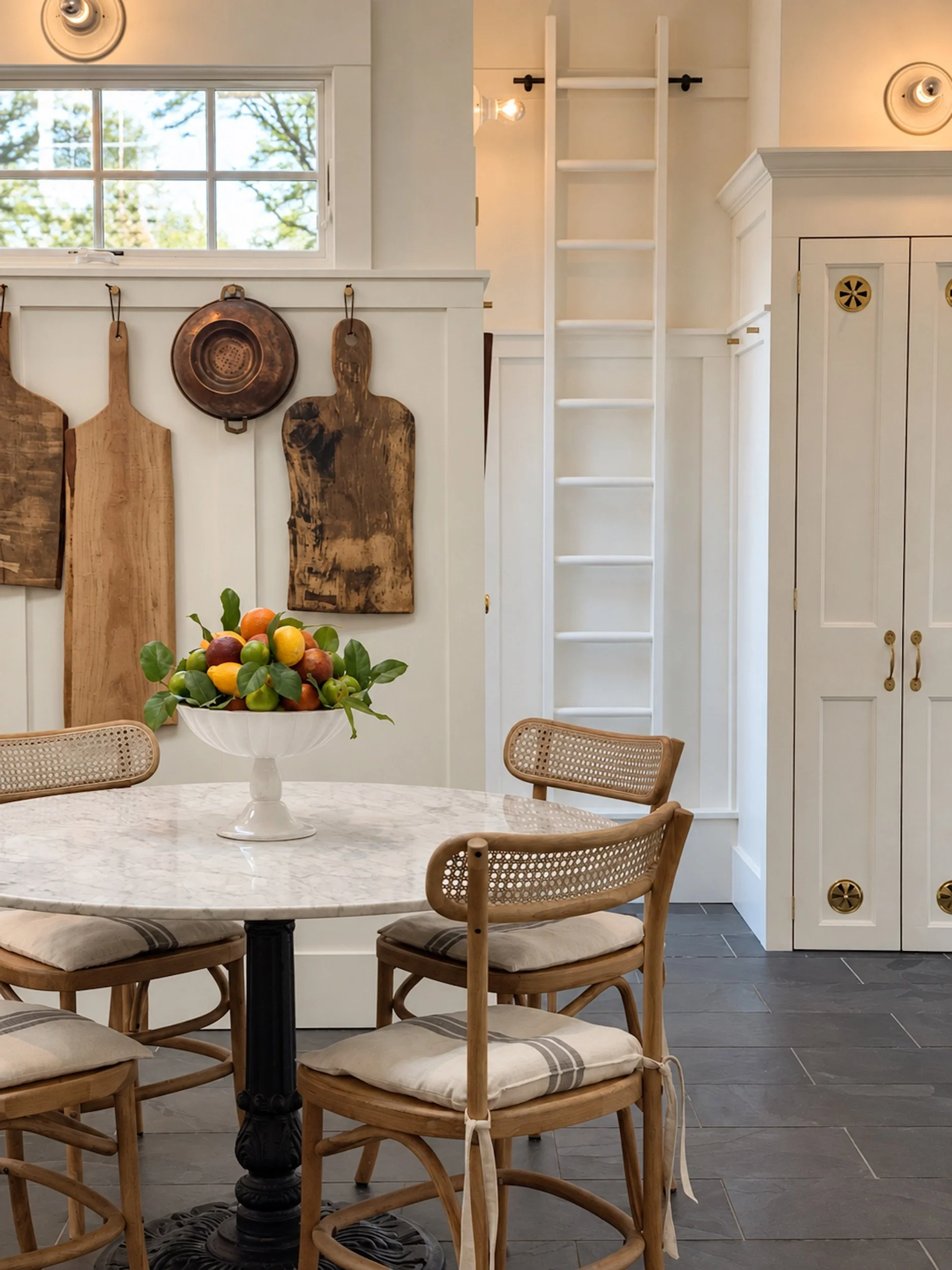 A kitchen with round marble table, hanging cutting boards and a ladder handing on the wall