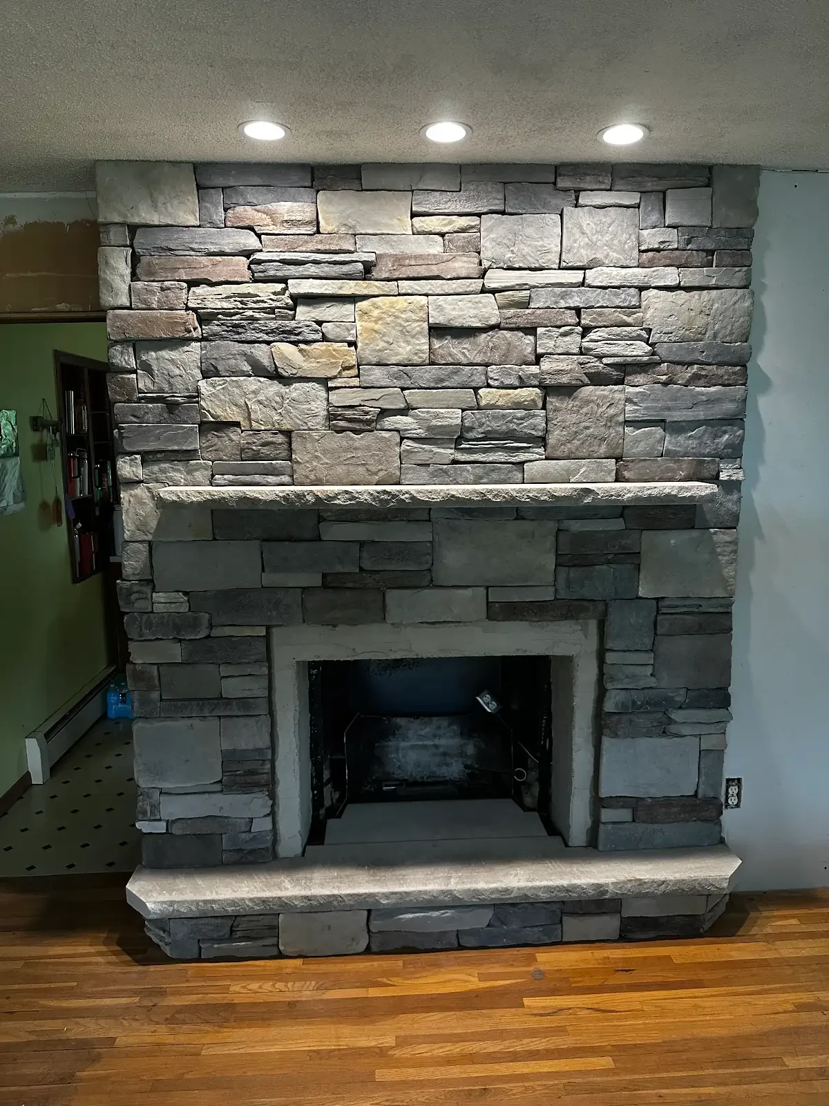 Stone fireplace with a mantel in a room with wooden flooring.