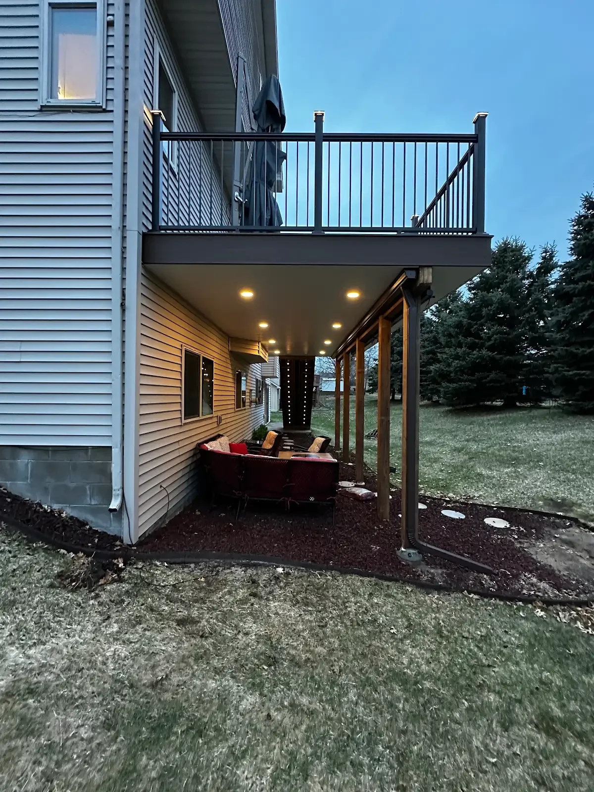 A house with a built-in covered patio area furnished with a sectional sofa, and a balcony above with a clothes hanging on the railing.