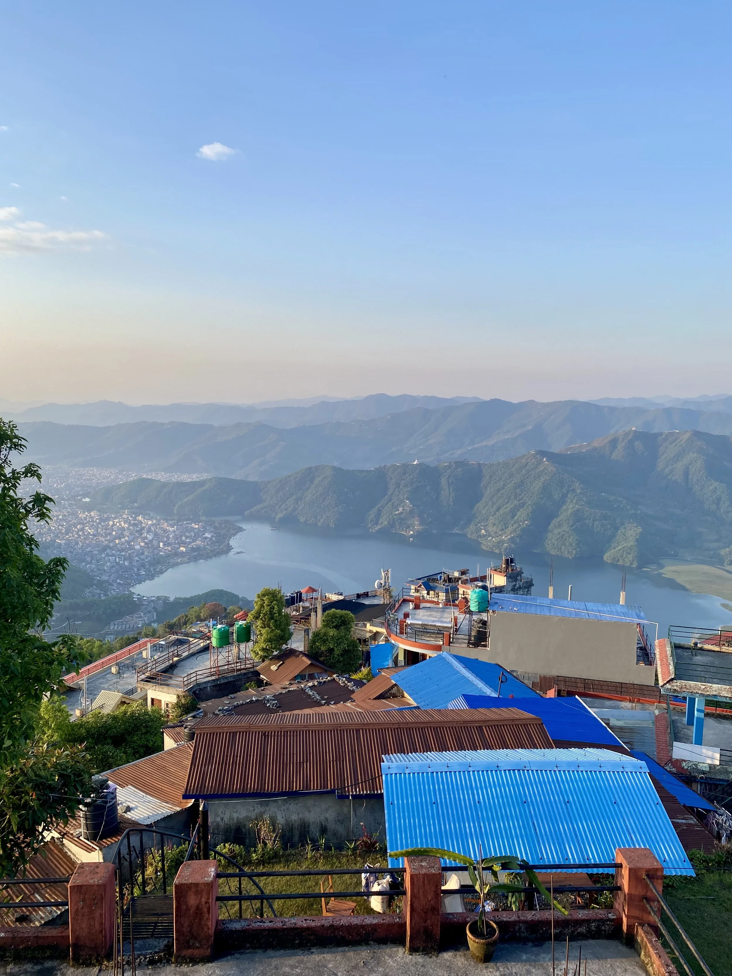 View of a residential area with colorful rooftops, a river, and mountains in the background under a clear blue sky.