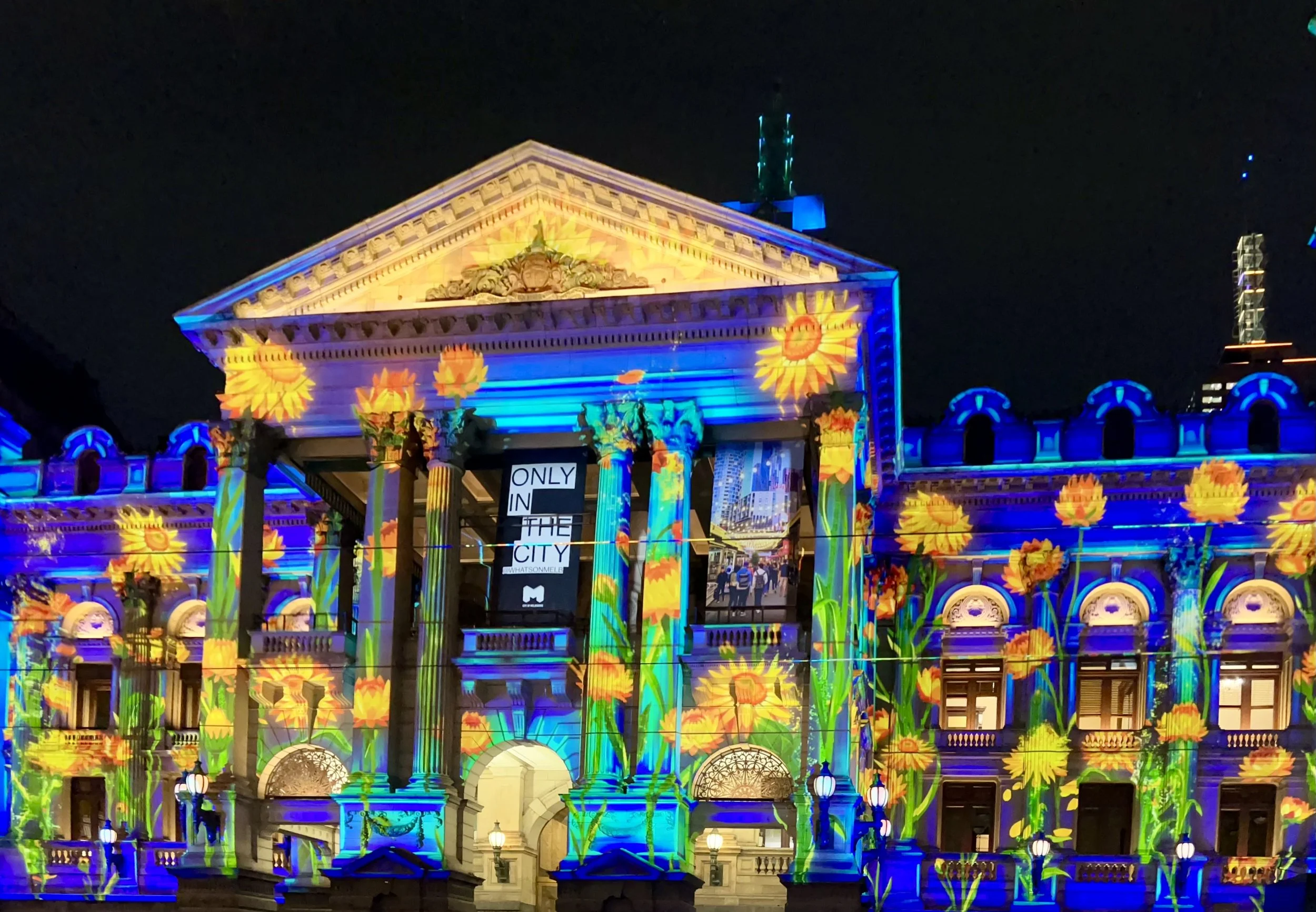 a building in melbourne illuminated with colourful sunflower projections at night.