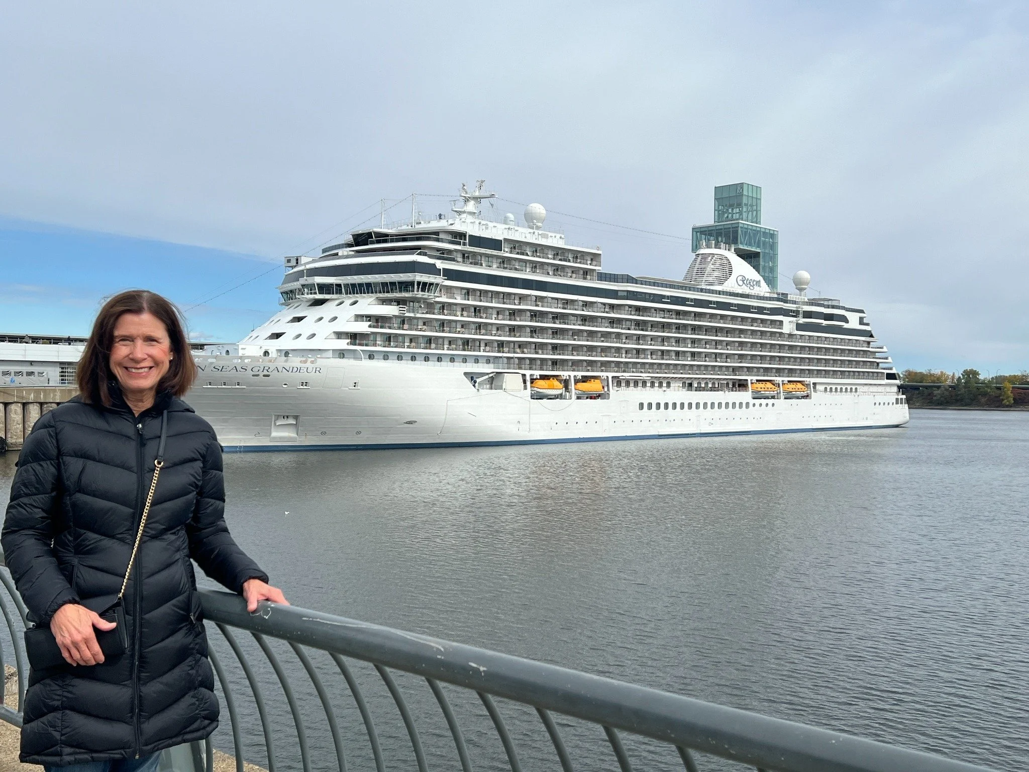 Kathy Stahl standing on a dock with a luxury cruise ship in the background.