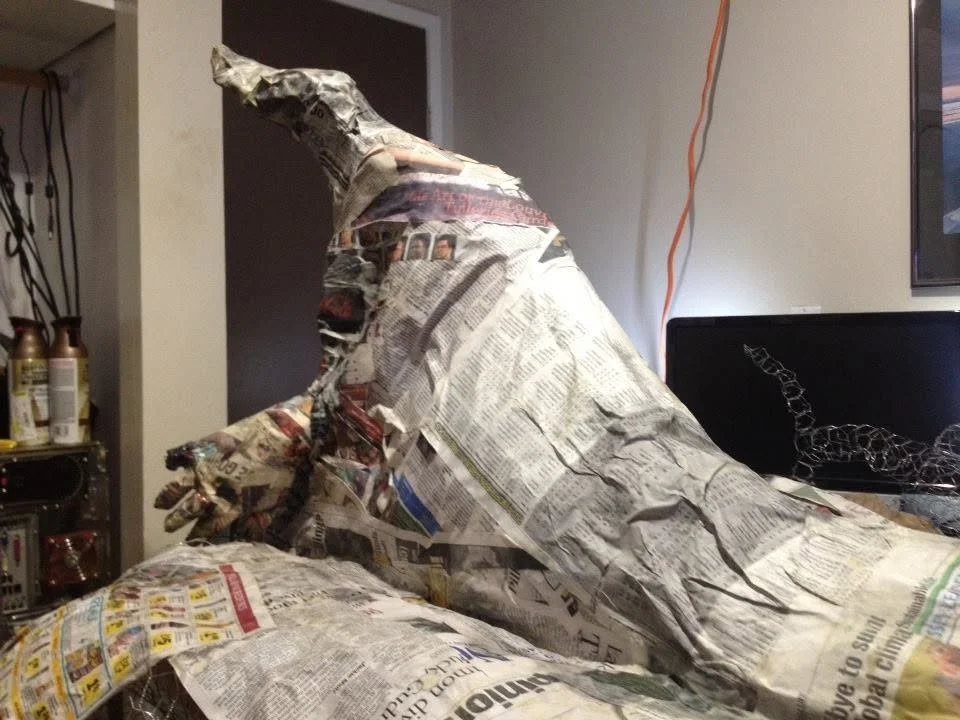 A sculpture of a T-Rex dinosaur made from crumpled and layered newspapers, positioned in a room.
