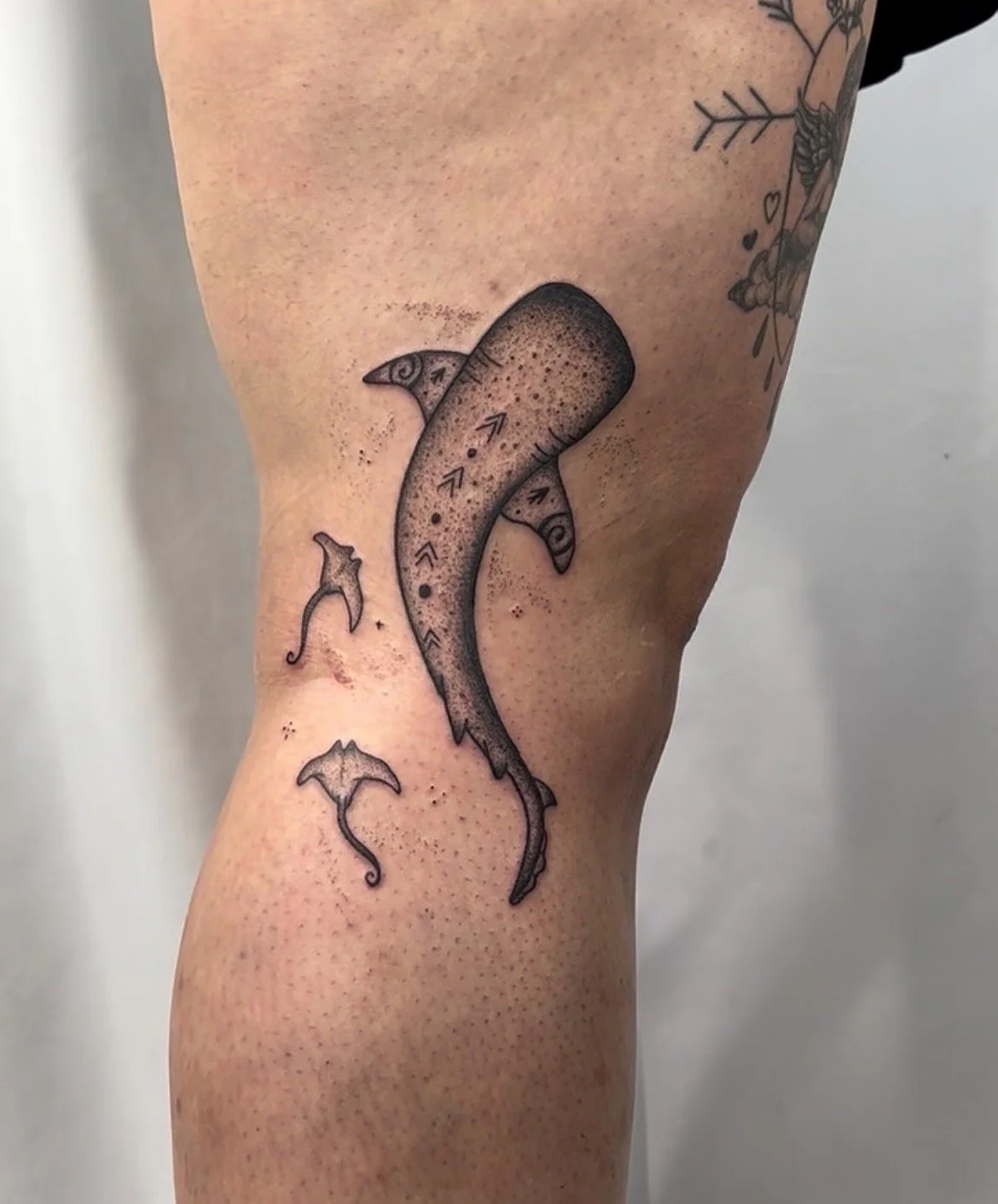 Tattoo of a stylized whale shark with geometric patterns and small sharks swimming around it on a person's upper arm.