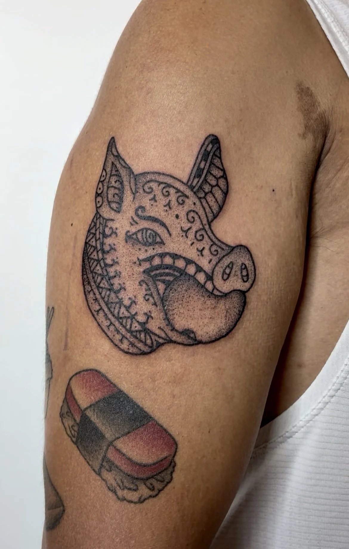 Tattoo of a pig's head with intricate patterns on the person's upper arm.