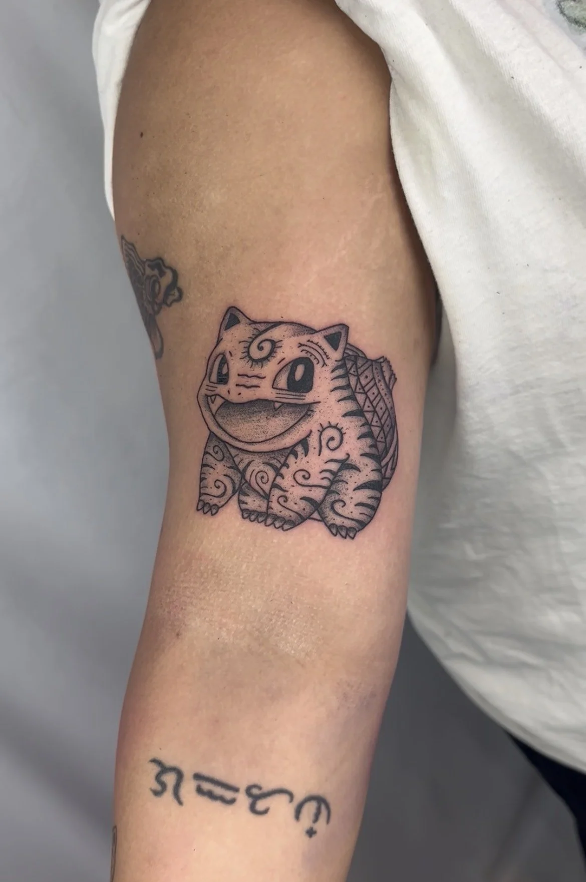 Tattoo of a cute, stylized tiger with detailed patterns, located on a person's upper arm.