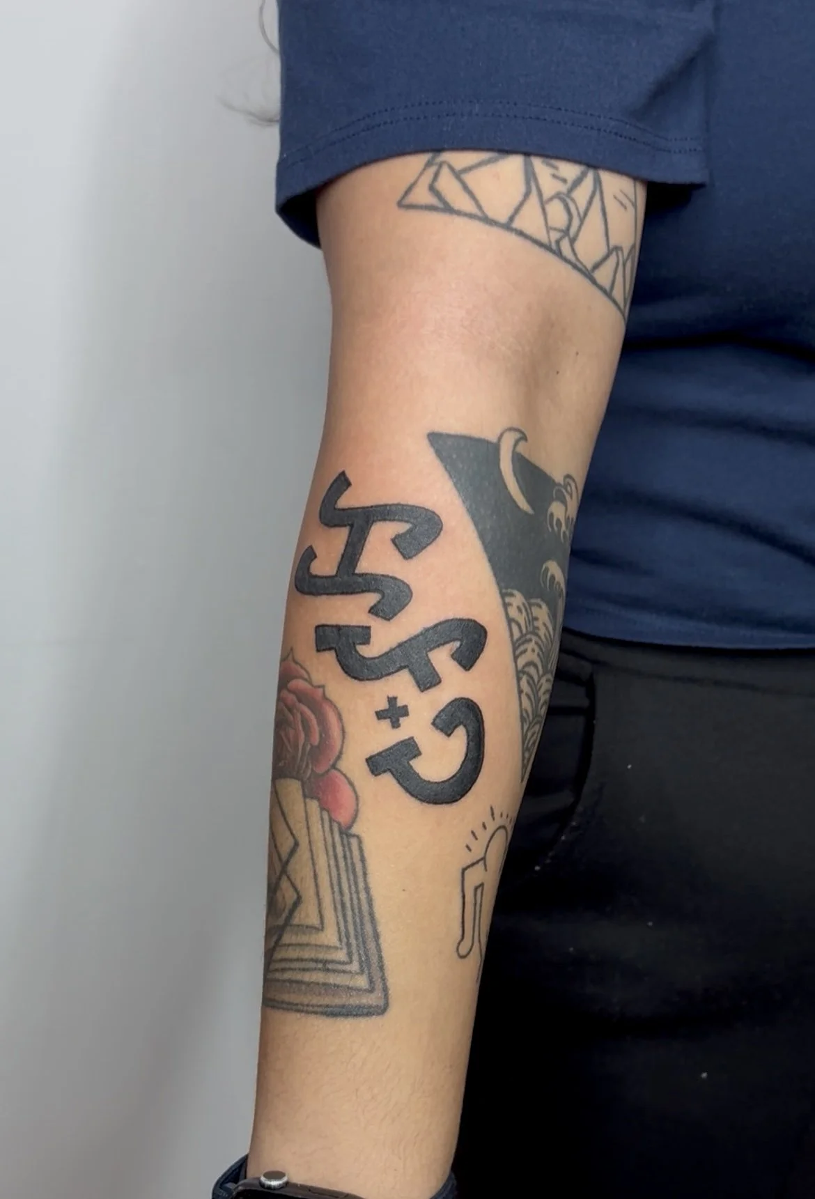 A person's arm with several tattoos, including black text reading 'RESCUE + CARE', a colorful rose, and a geometric pattern near the shoulder. The person is wearing a blue shirt with the sleeve rolled up.