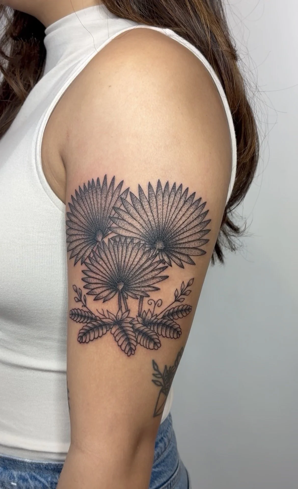 Close-up of a woman's upper arm with a black outline tattoo of three large daisies and leaves.