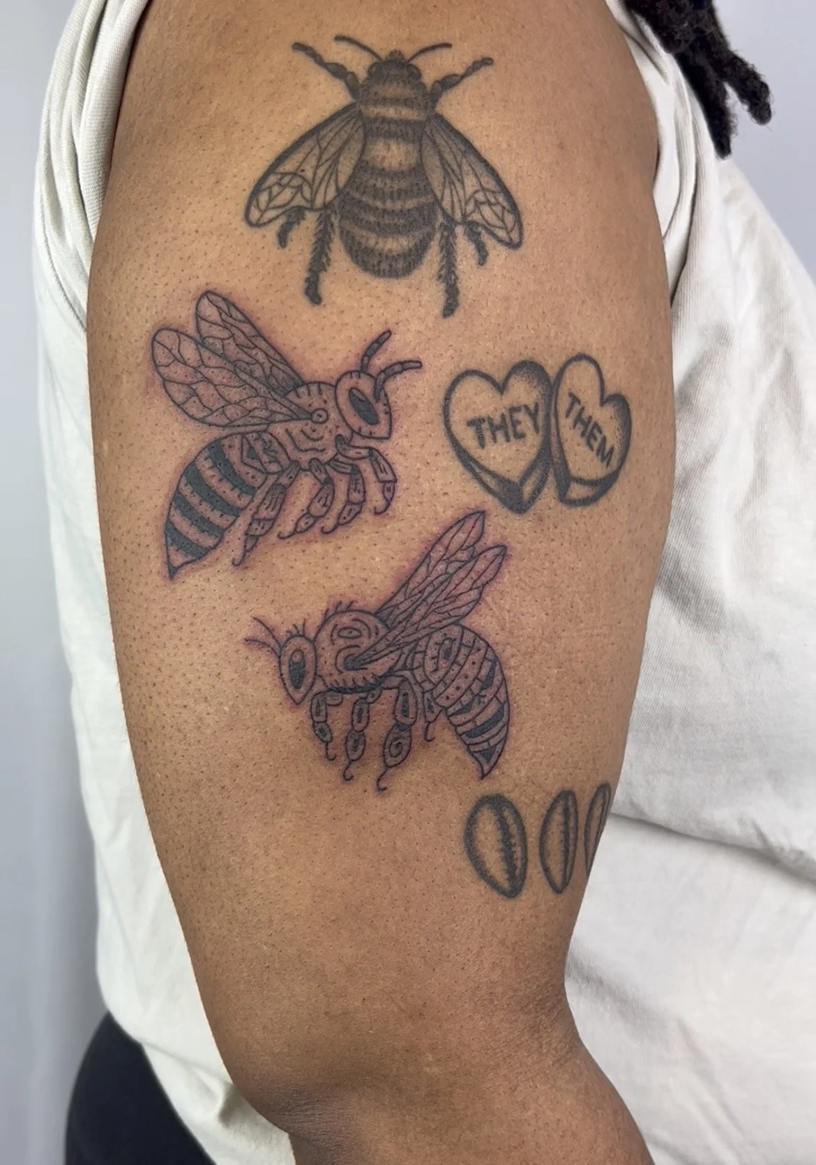 Tattoo of three bees and a heart with the words "They" and "Them" on a person's upper arm.