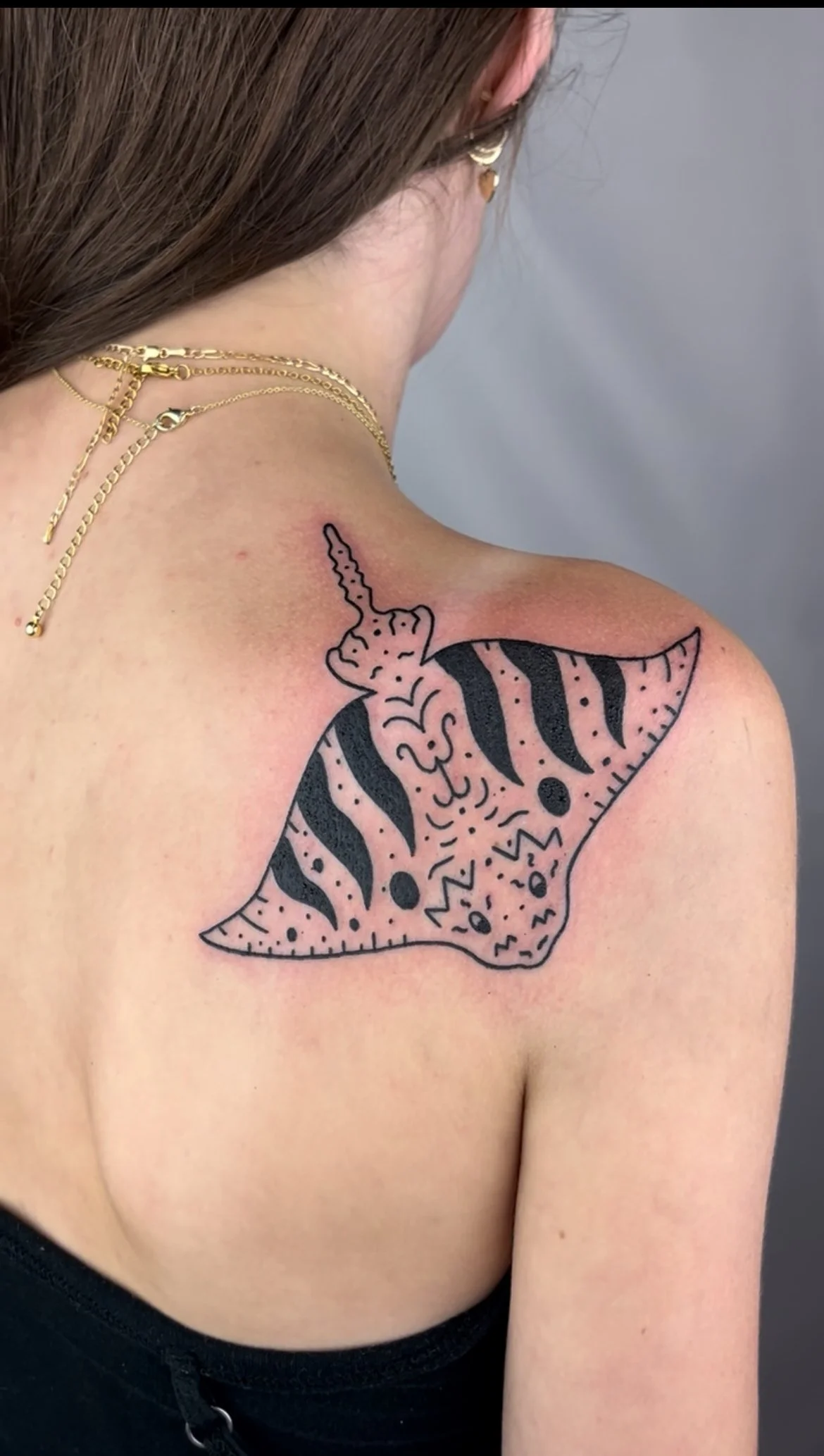 Tattoo of a stylized tiger on the woman's shoulder and upper arm, with black and pink details, and jewelry including gold necklaces.