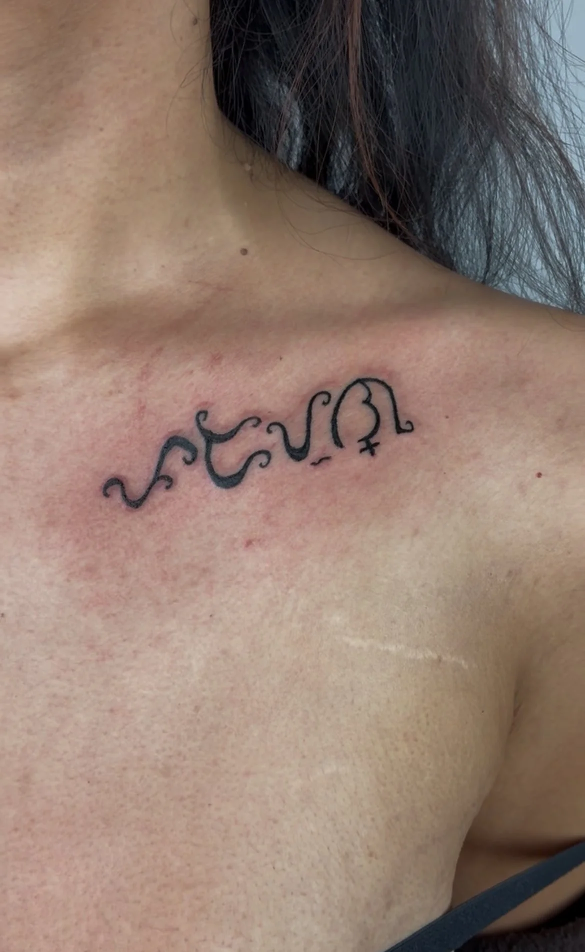 A tattoo of the word 'love' written in cursive on a person's upper chest near the collarbone.