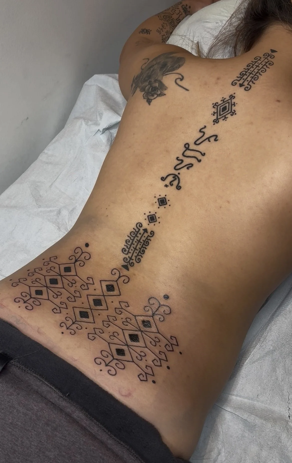Close-up of a person's arm with intricate black Filipino and ornamental tattoos, lying on a white surface.