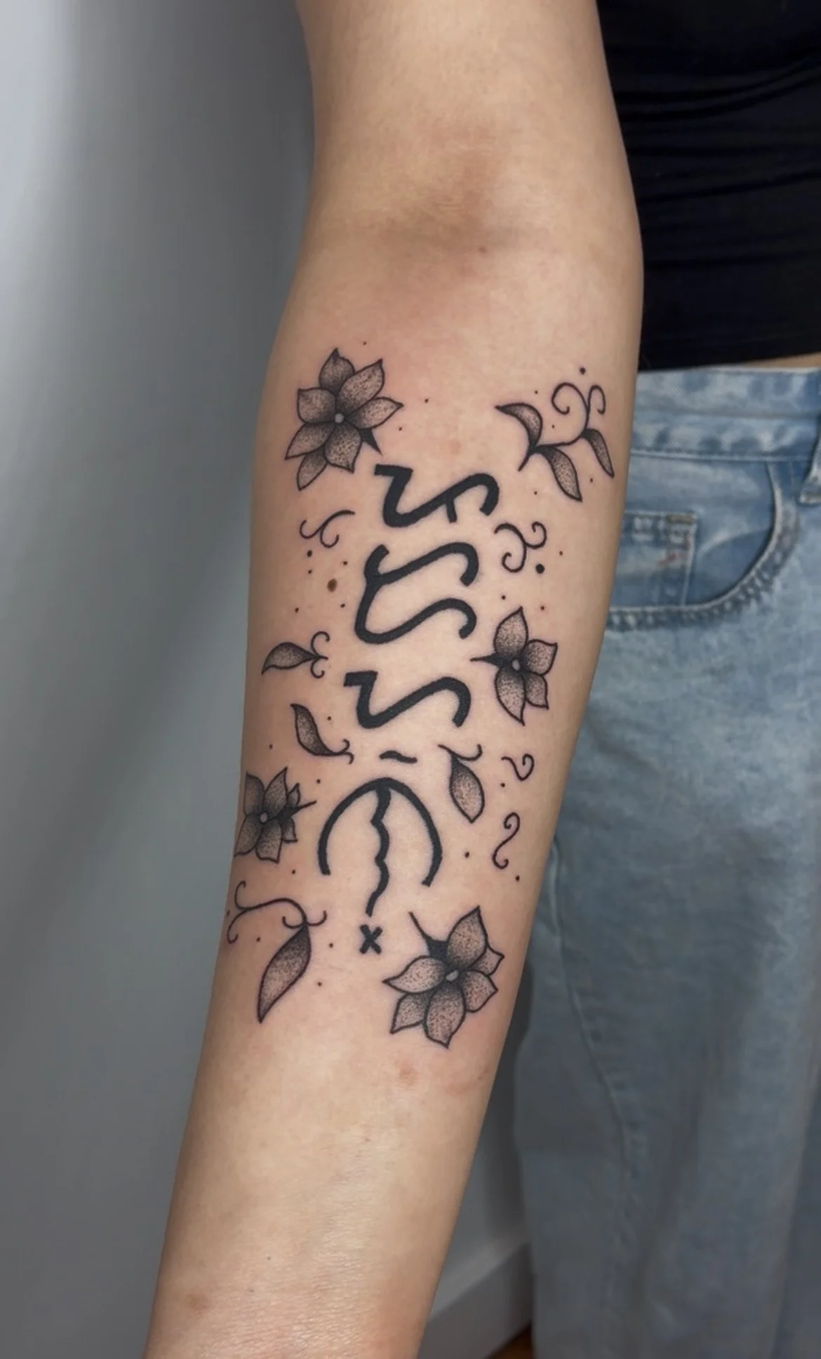 Tattoo on person's forearm with floral designs and the word "Sun" written vertically.