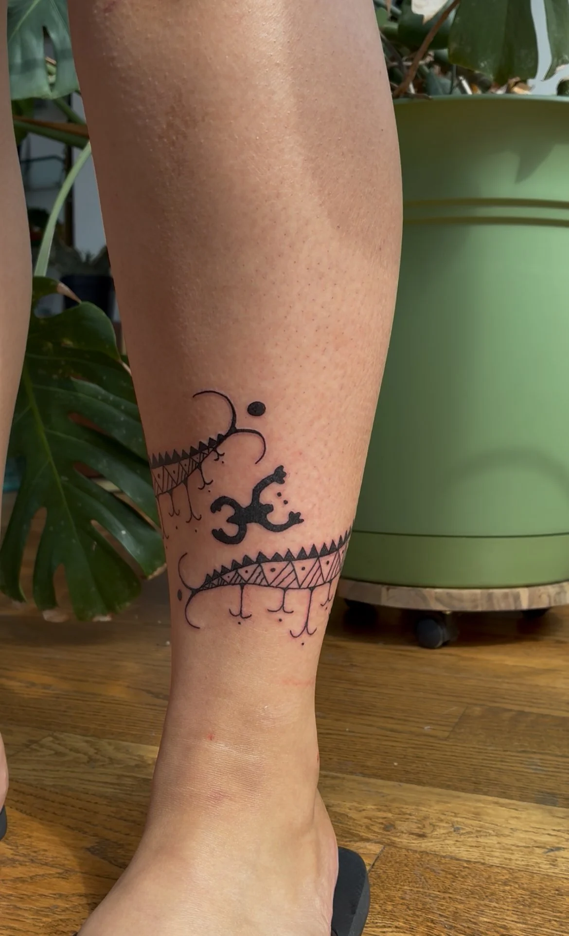 Tattoo on person's lower leg featuring a black infinity symbol, a lizard, and decorative patterns.