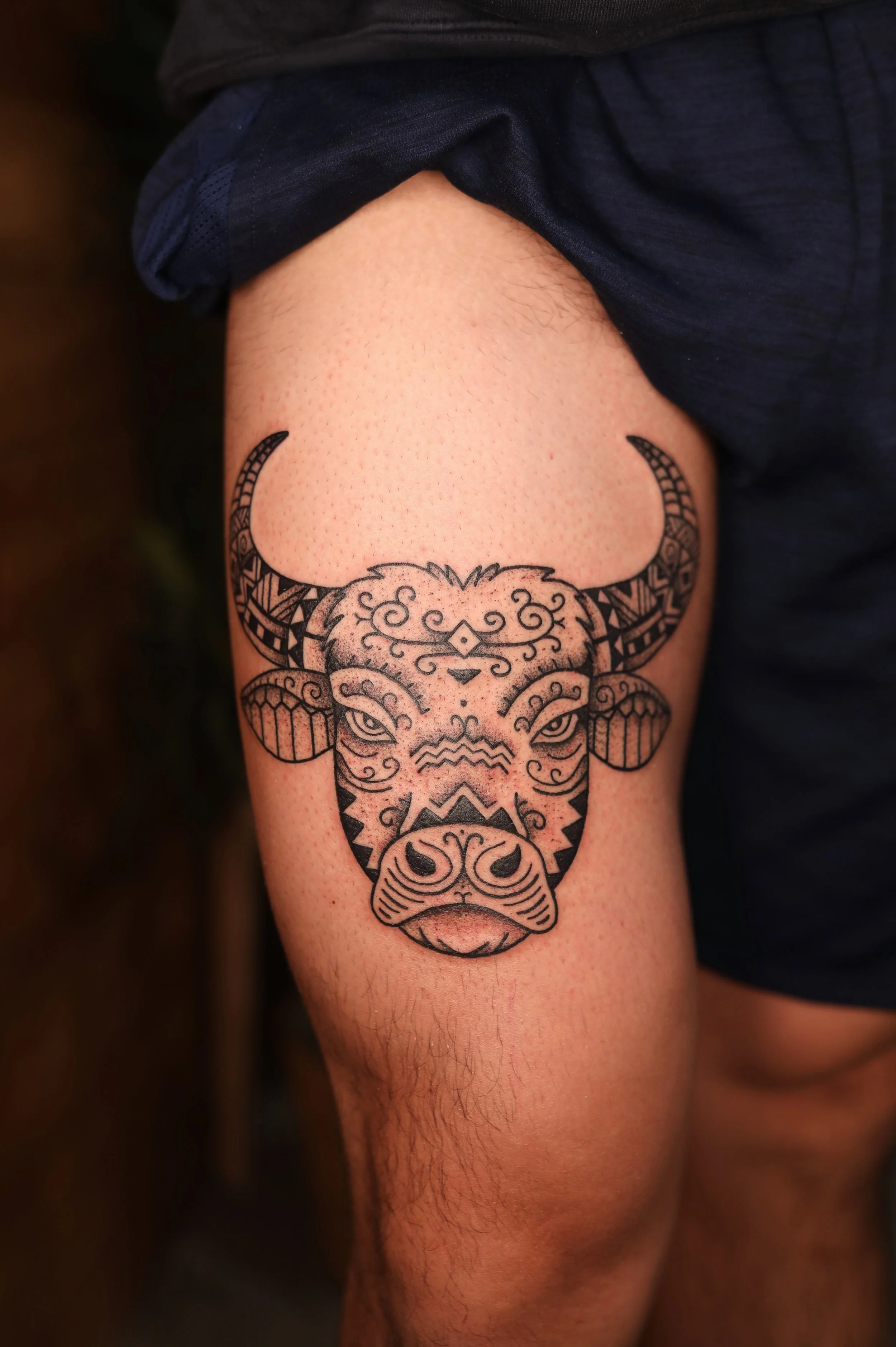 A tattoo of a buffalo head on a person's upper arm, featuring detailed line work and geometric patterns.