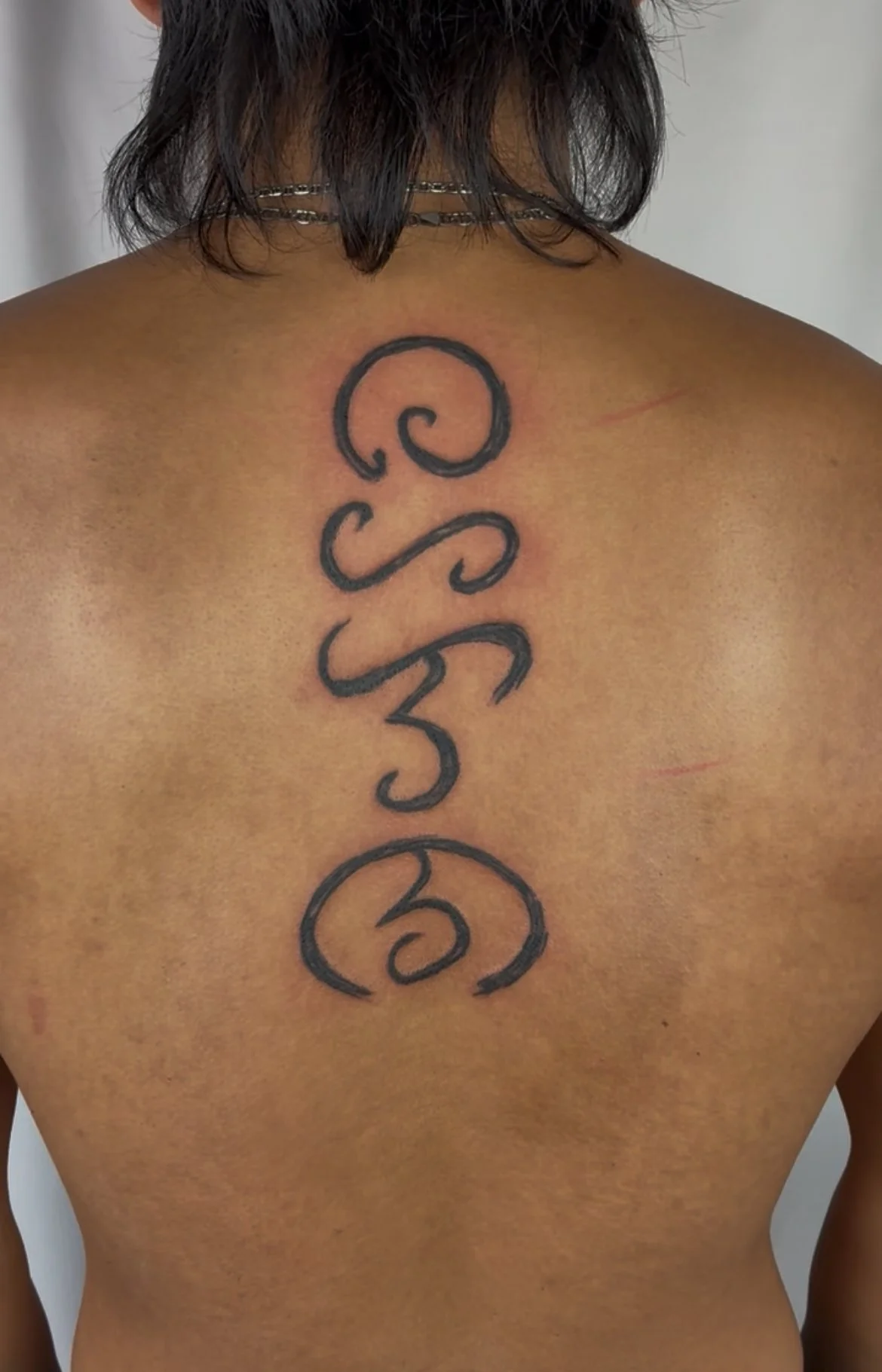 Back of a person's upper body with a tattoo of the word 'blessed' written vertically in black cursive letters.