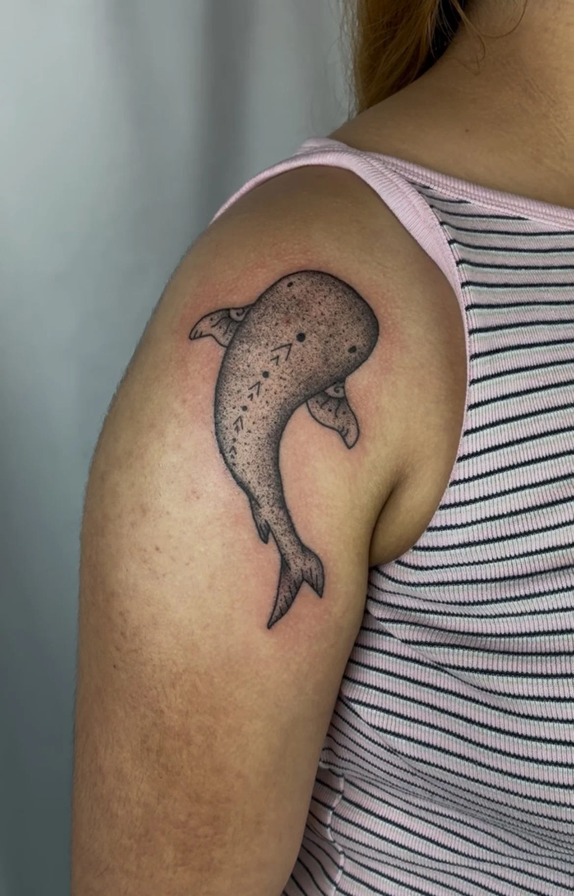 A tattoo of a whale on a person's shoulder featuring detailing and arrows indicating shading or design elements.