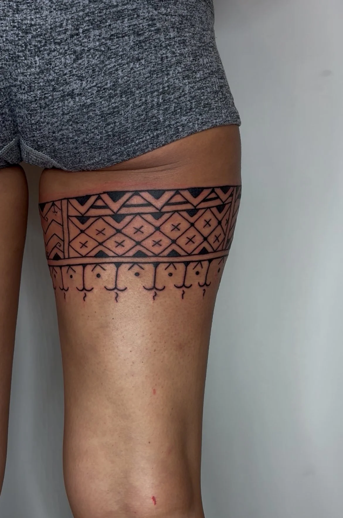 Close-up of a person's upper thigh and hip with a detailed black geometric and tribal tattoo design.