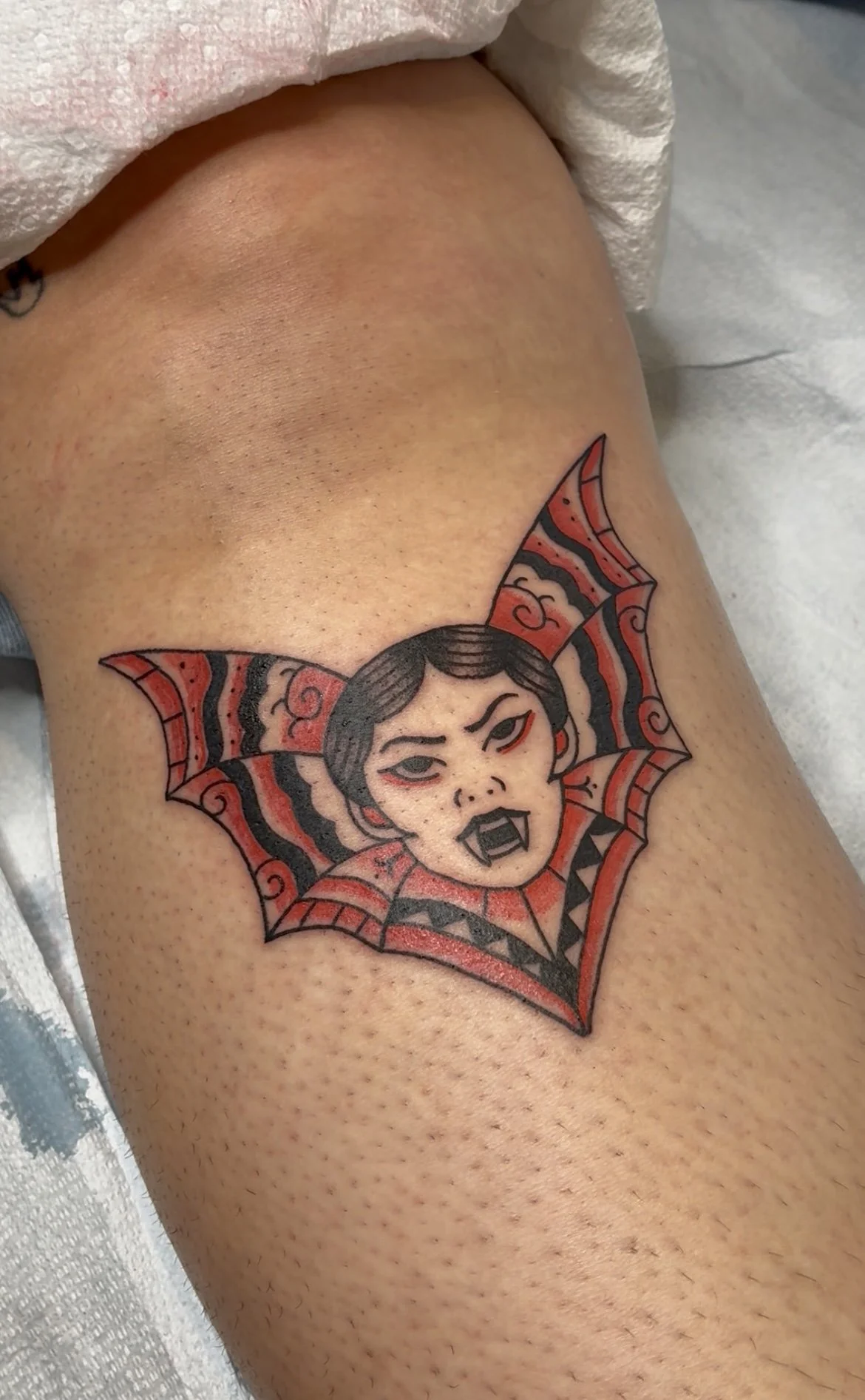 Tattoo of a manamangal with bat wings on her head, fangs, and a fierce expression on the thigh.
