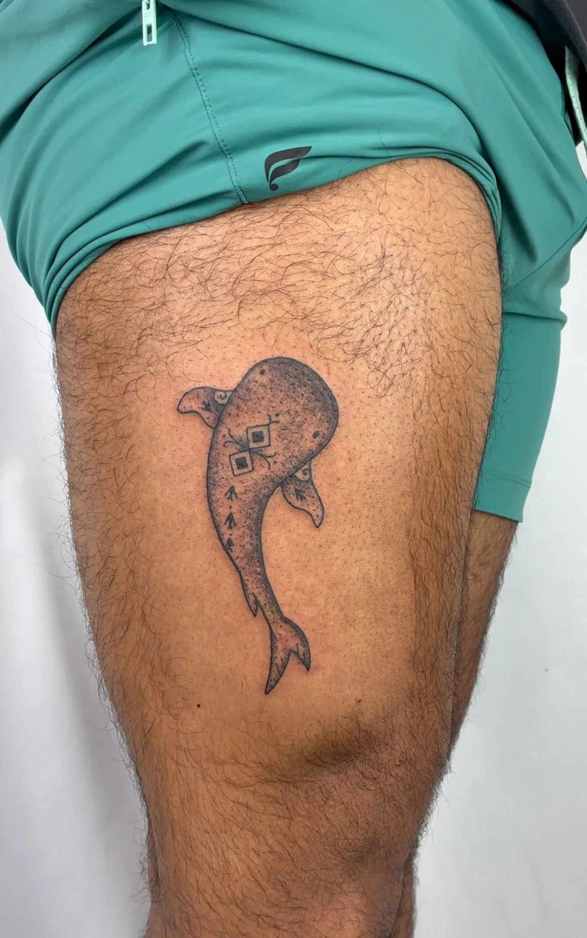 Tattoo of a dolphin on a person's thigh with a dotted shading style, arrows indicating movement, and small geometric details.