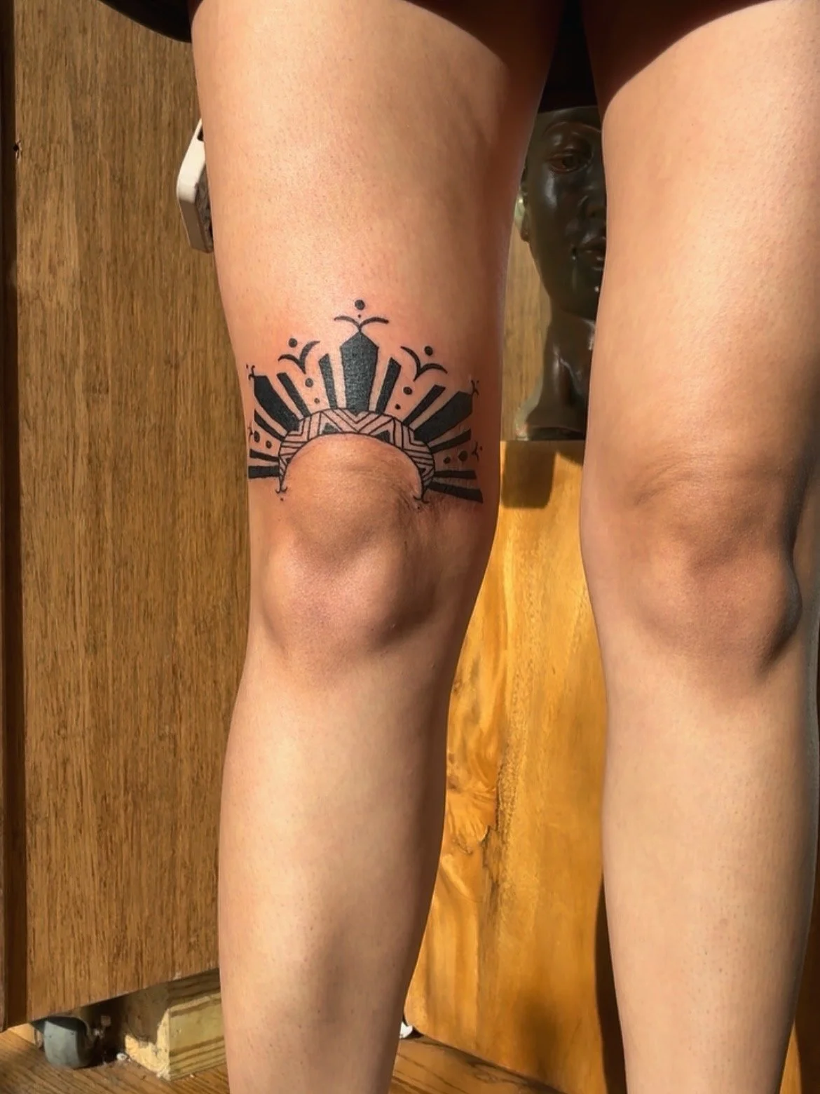 Tattoo on the left thigh of a person, depicting a stylized sun with radiating rays and geometric elements.