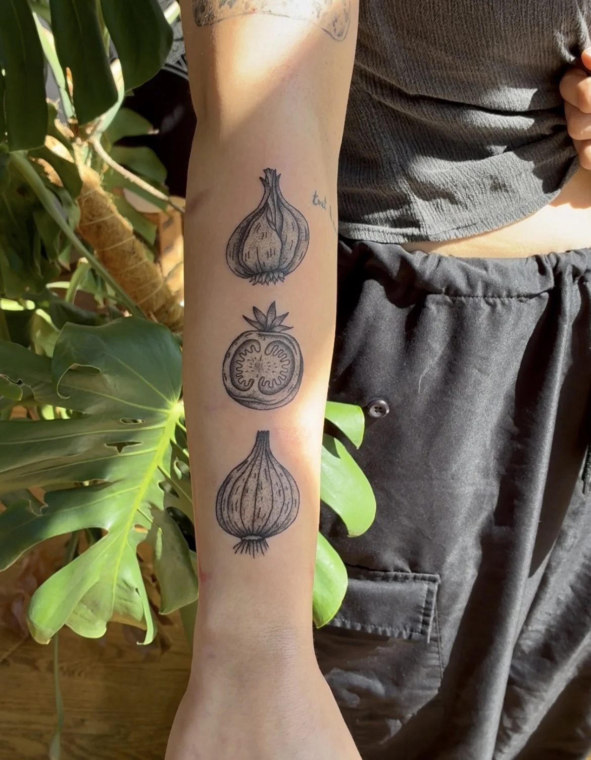 Tattoo of a garlic bulb, a tomato cross-section, and a onion on a person's forearm.