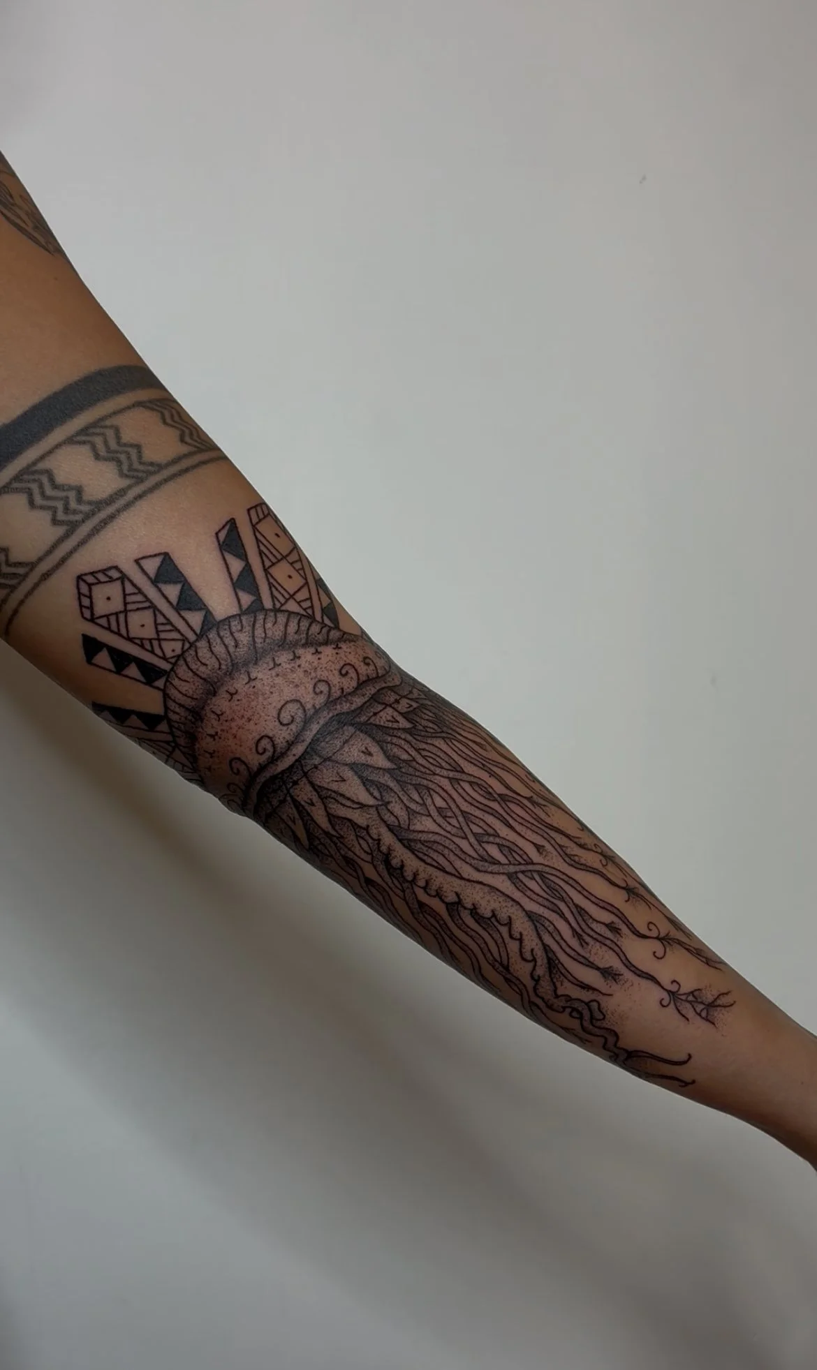Close-up of a person's arm with a detailed black and grey tattoo featuring geometric patterns, a circular motif, and intricate lines.