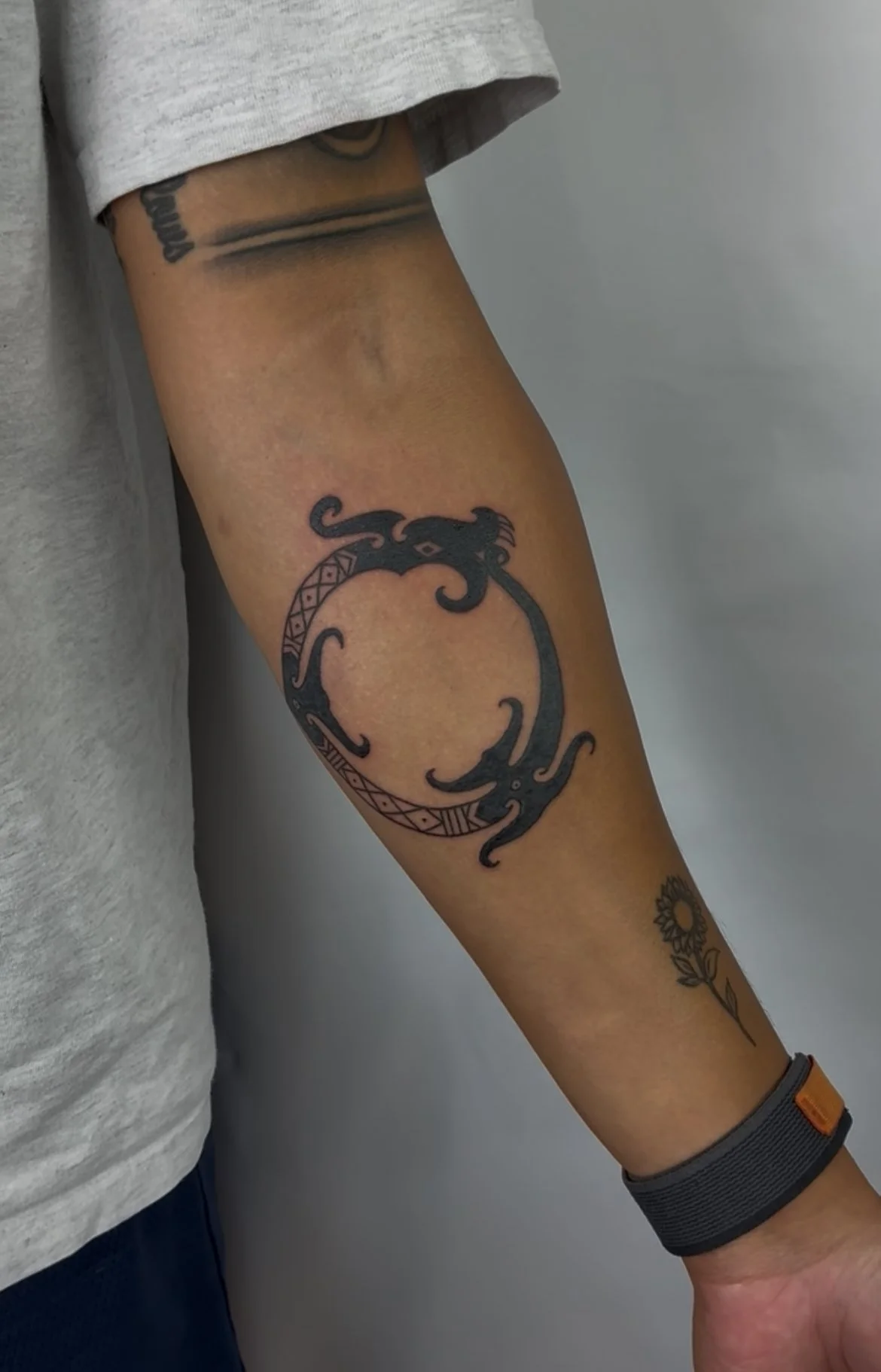 Tattoo of two black tribal-style lizards forming a circle on a person's upper arm.