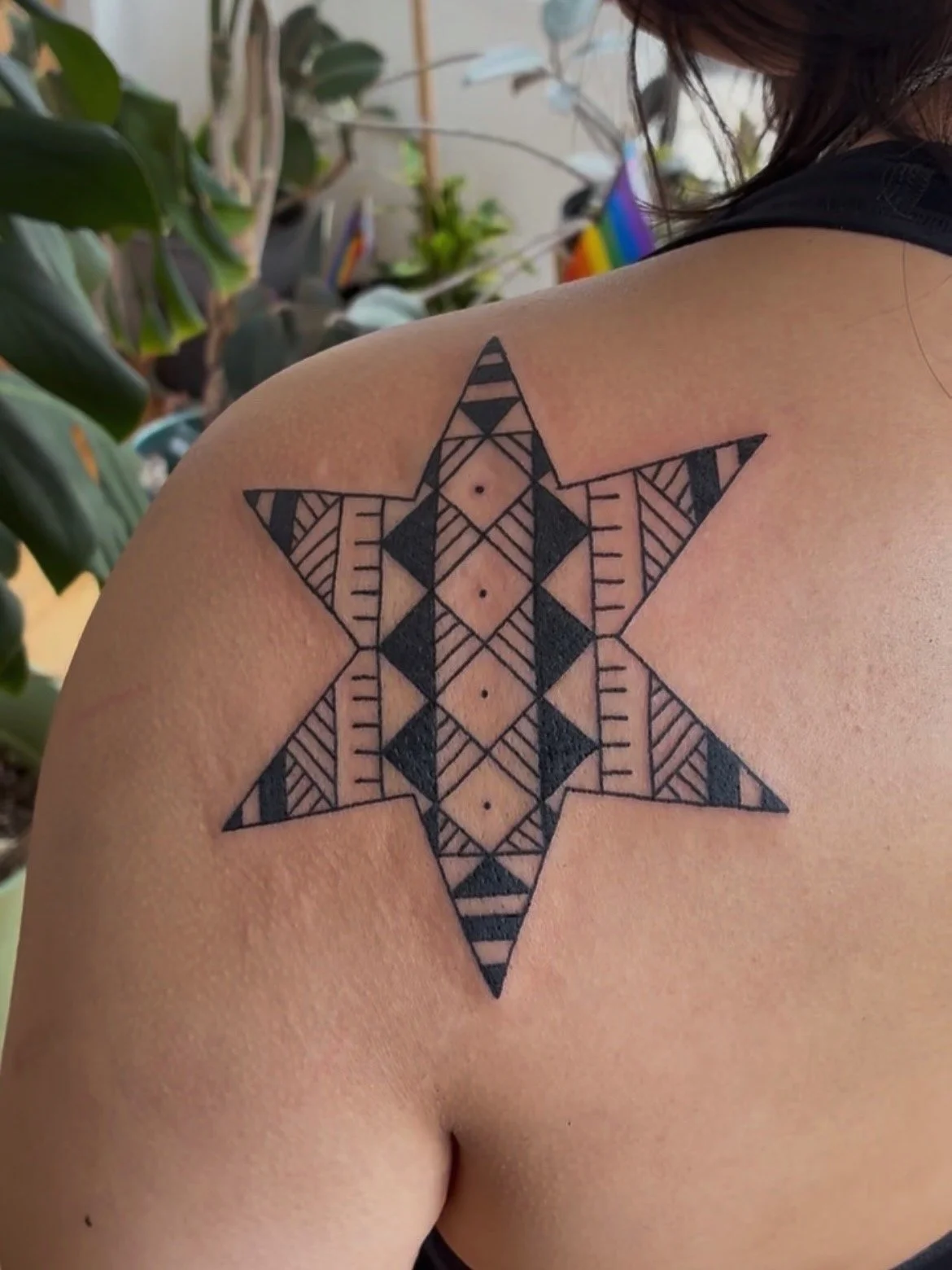 A geometric star-shaped tattoo on a person's shoulder, featuring various patterns in black ink.