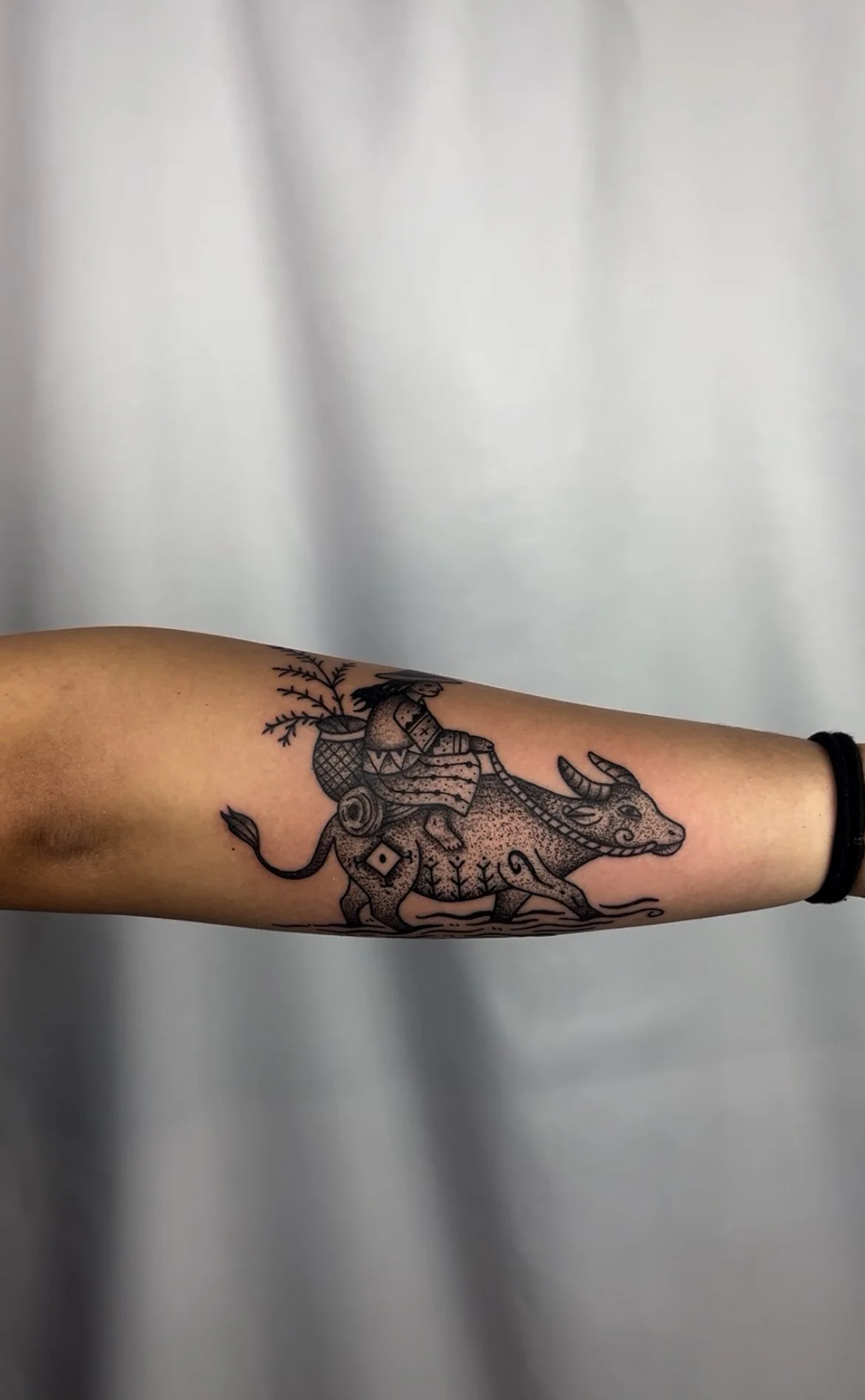 Tattoo of a person carabao with ornaments and plants in the background on a person's arm.