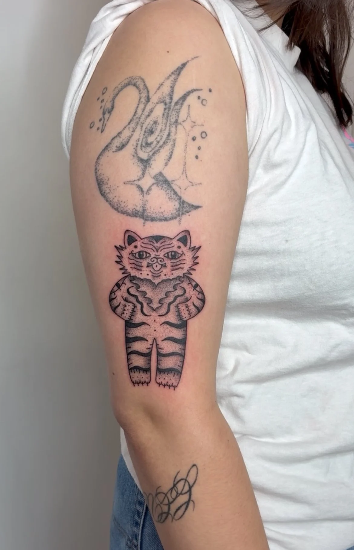 Two tattoos on a person's upper arm: an outlined crescent moon and stars with a splash effect on top, and a stylized panda bear with tiger stripes below.
