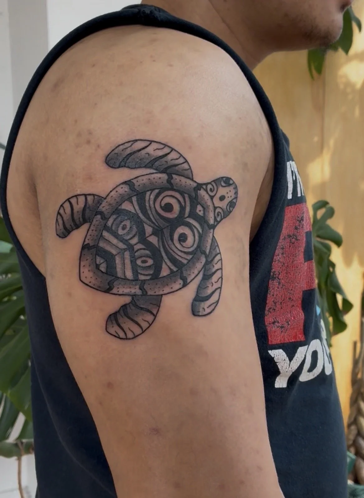 Tattoo of a stylized, tribal-inspired sea turtle on a person's upper arm.