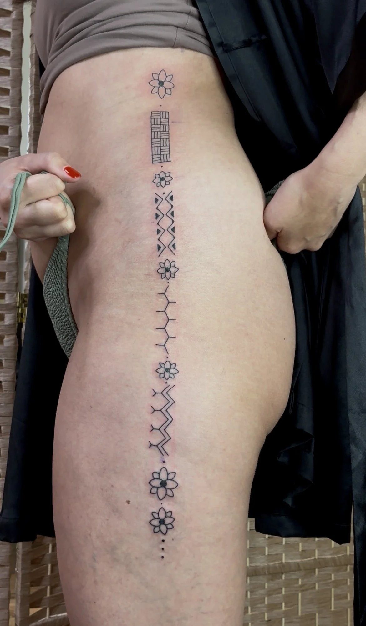 A person's side with a tattoo running from their ribcage to their thigh, featuring flowers, geometric patterns, and lines.