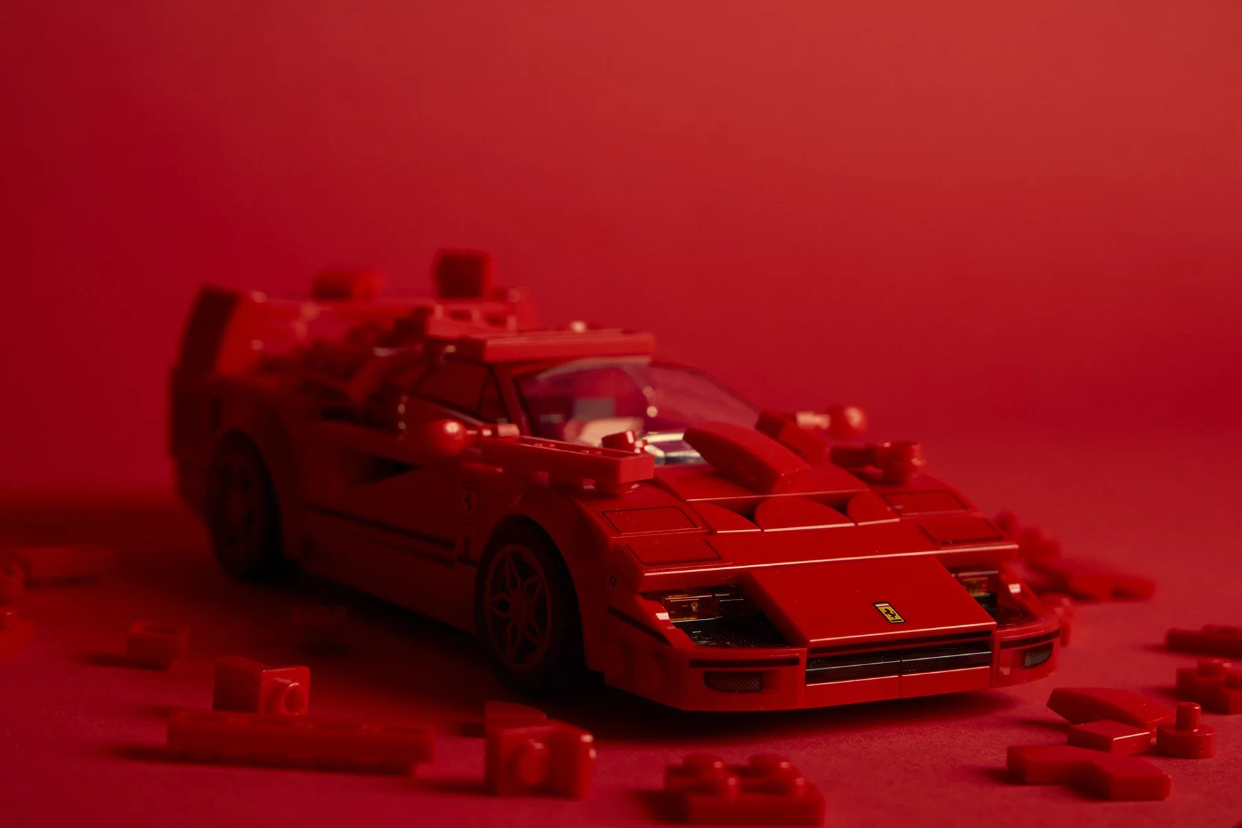 A red LEGO Ferrari sports car model displayed against a red background, surrounded by scattered red LEGO bricks.