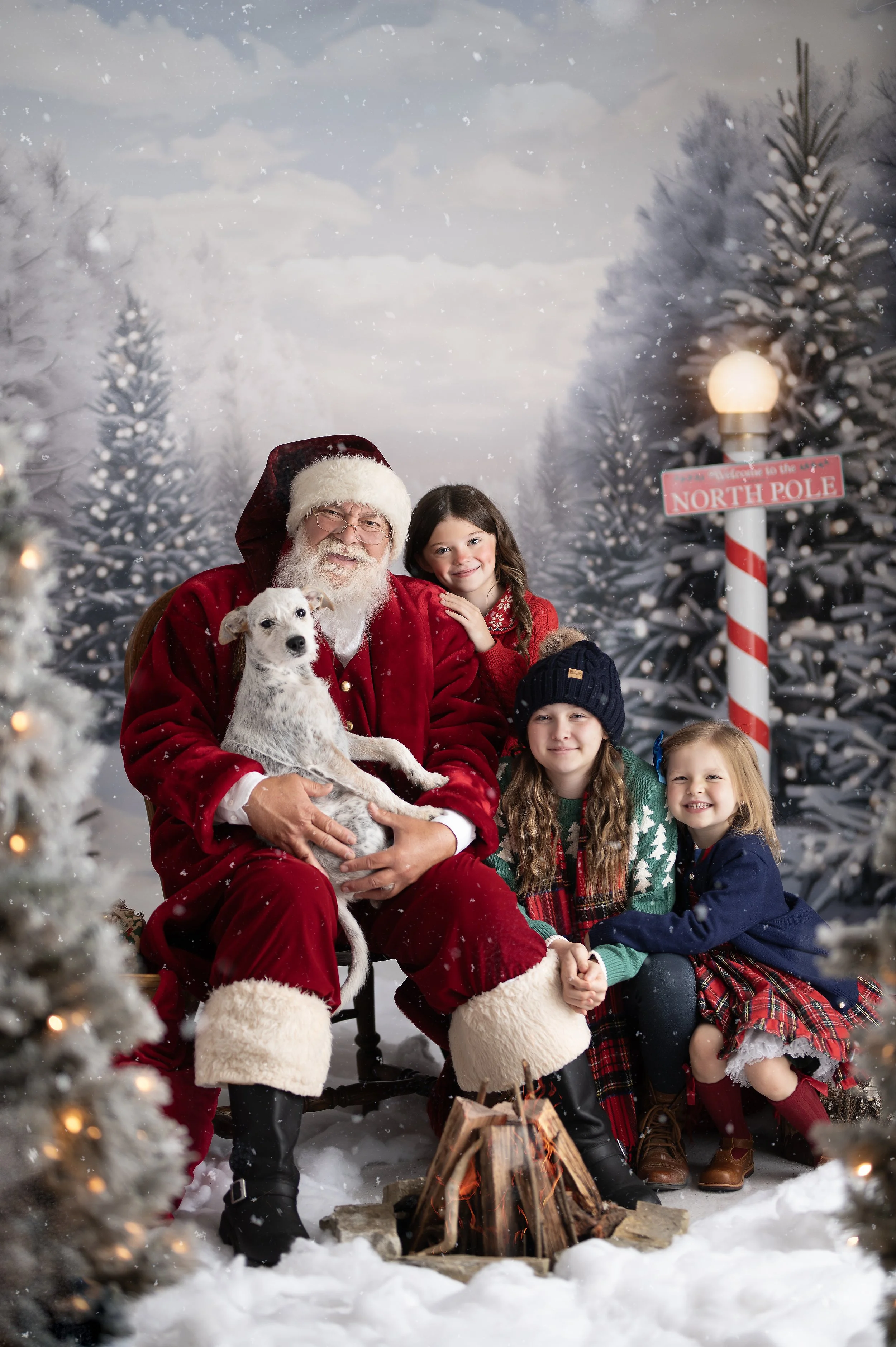 Santa posing with three children and their dog in a snowy Christmas photography set.