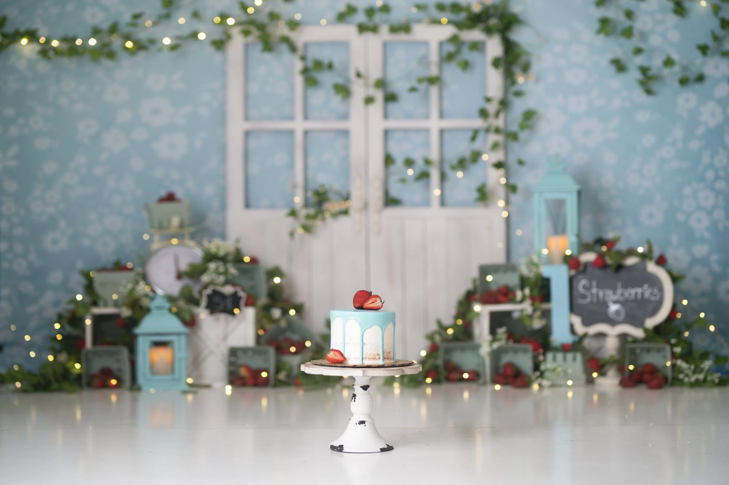 Soft blue and greenery Cake Smash photography set featuring lanterns, floral details, and a birthday cake.