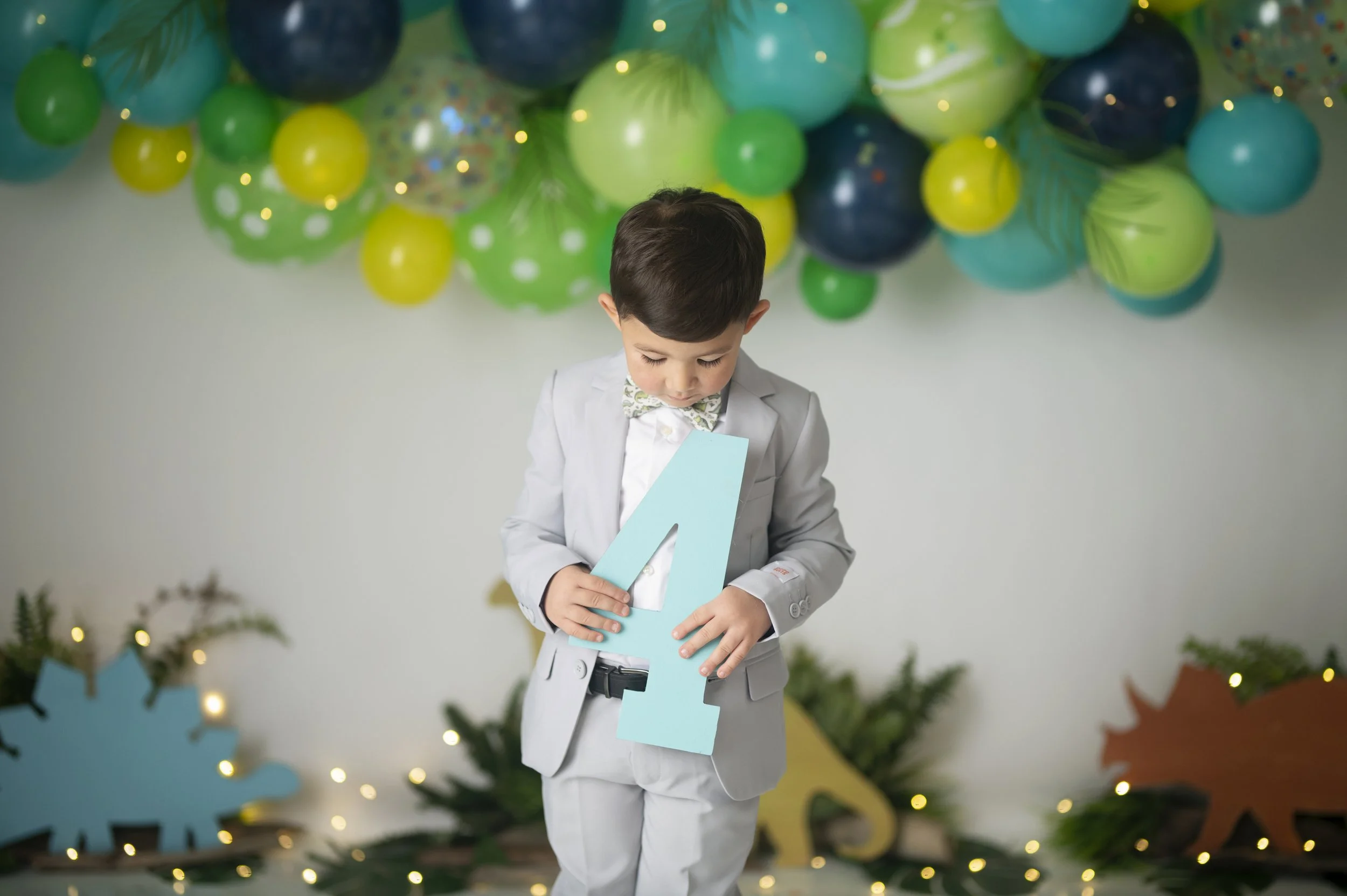 Young boy holding a number four in front of a colorful balloon backdrop during a milestone session.