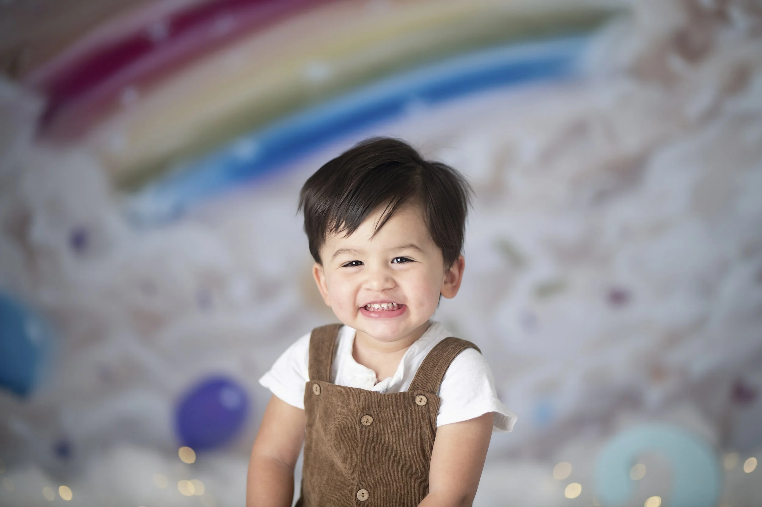 Smiling young child posing in front of a colorful rainbow backdrop during a birthday photography session.
