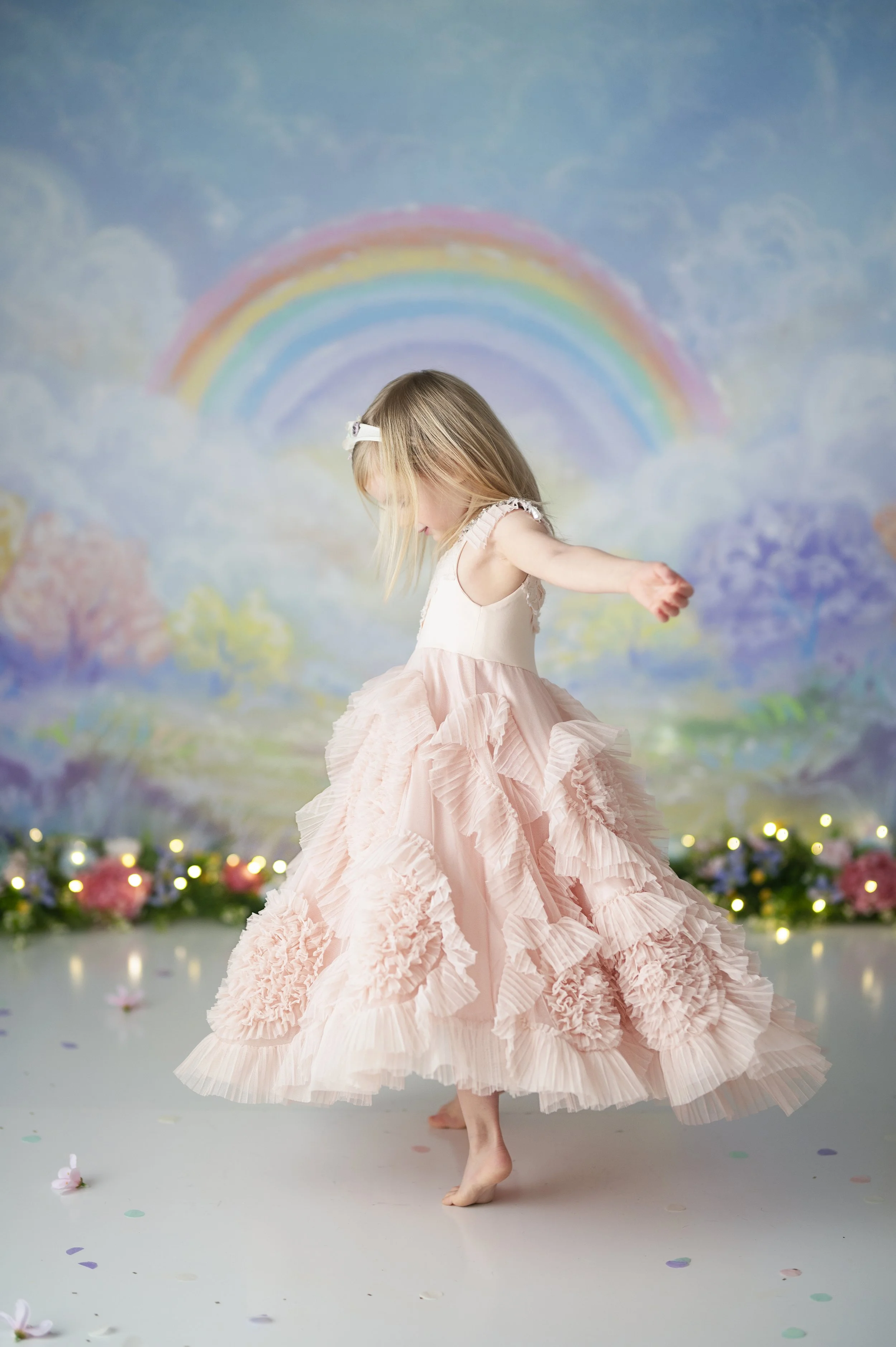 Young girl twirling in a pink dress in front of a pastel rainbow photography backdrop.