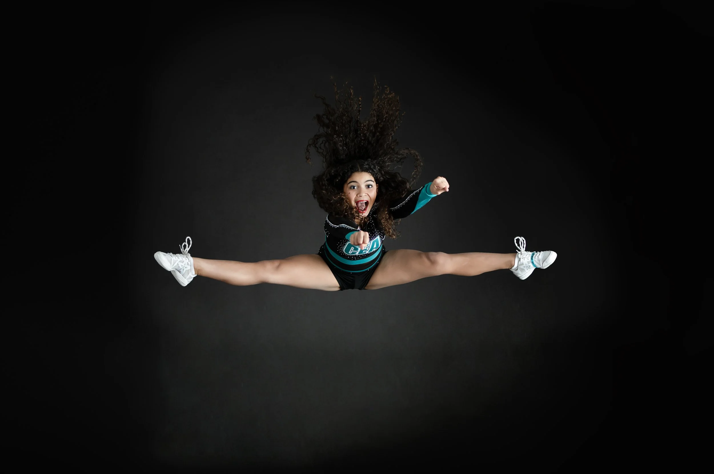 Cheer athlete performing a toe-touch jump against a dark studio background.