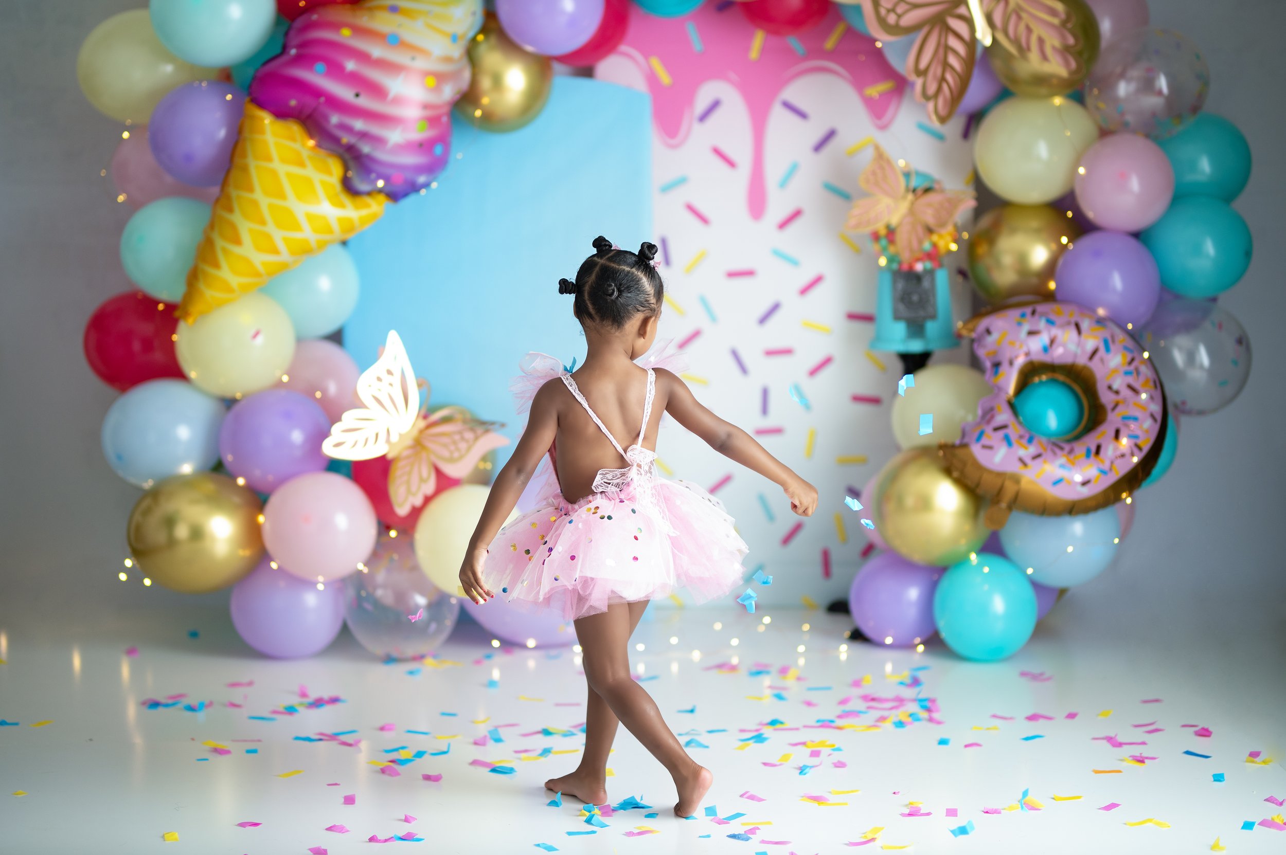 Young girl posing in a colorful ice cream and sprinkle-themed birthday photography set.