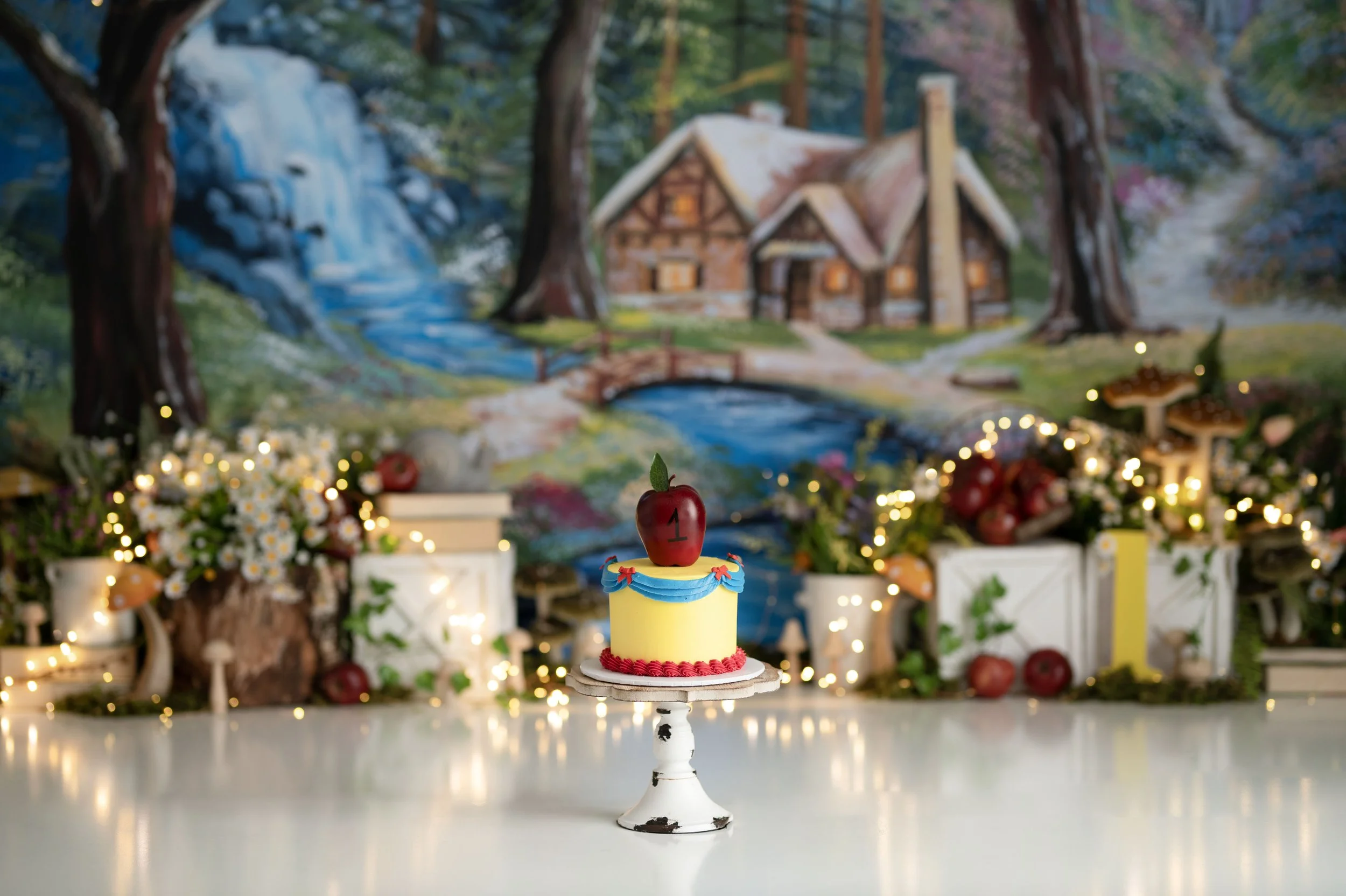 Storybook-inspired Cake Smash set featuring a woodland cottage backdrop, greenery, lights, and a colorful birthday cake.