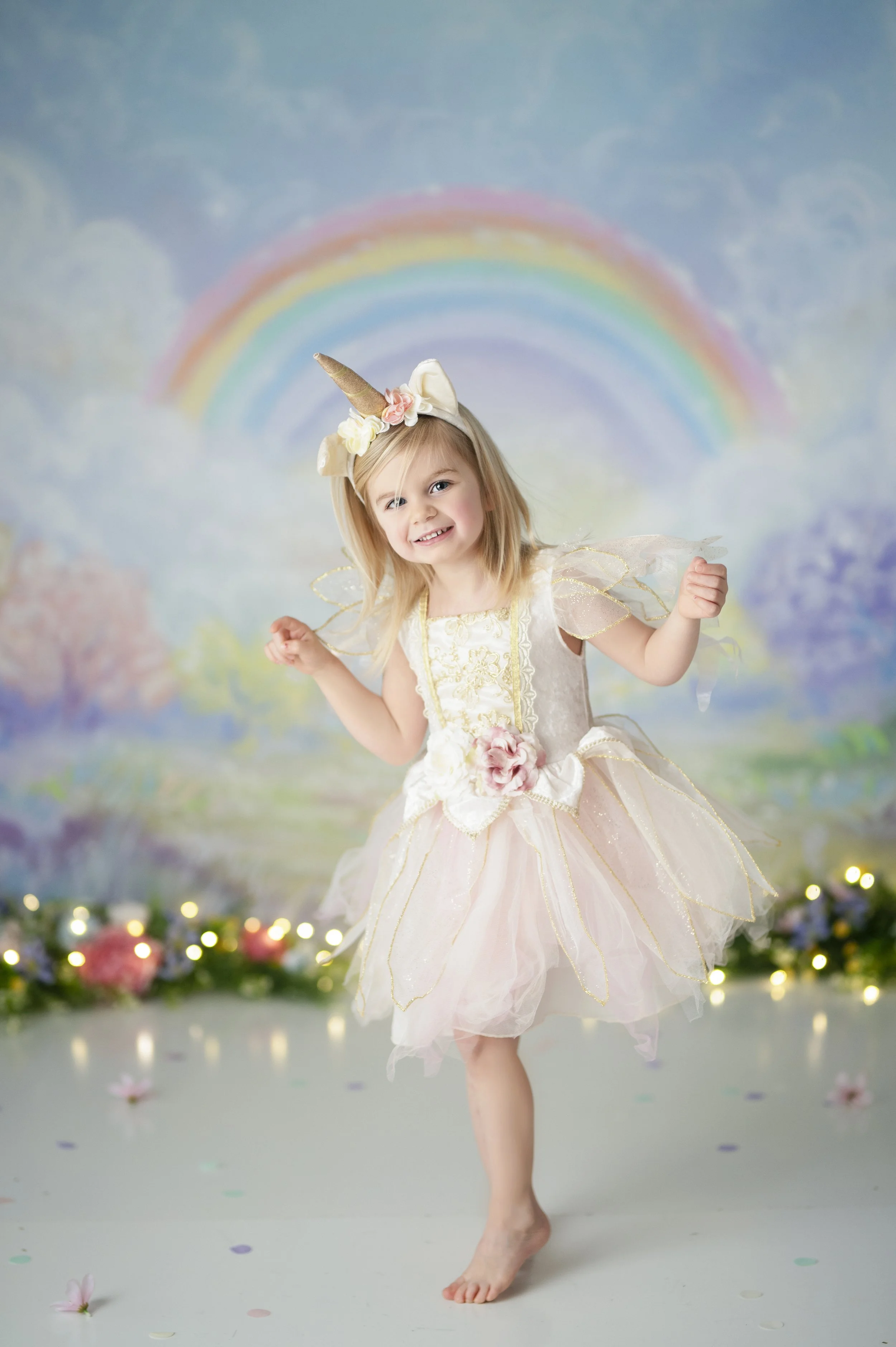 Young girl wearing a unicorn dress in front of a pastel rainbow photography backdrop.