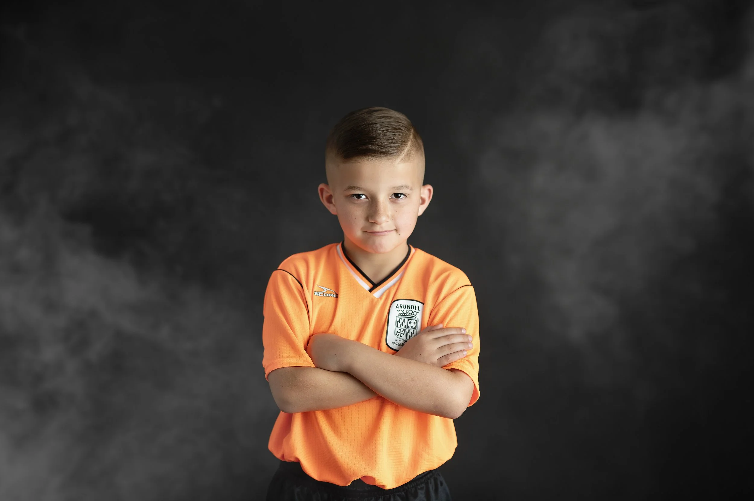 Youth soccer player posing in an orange uniform during a studio sports portrait session.