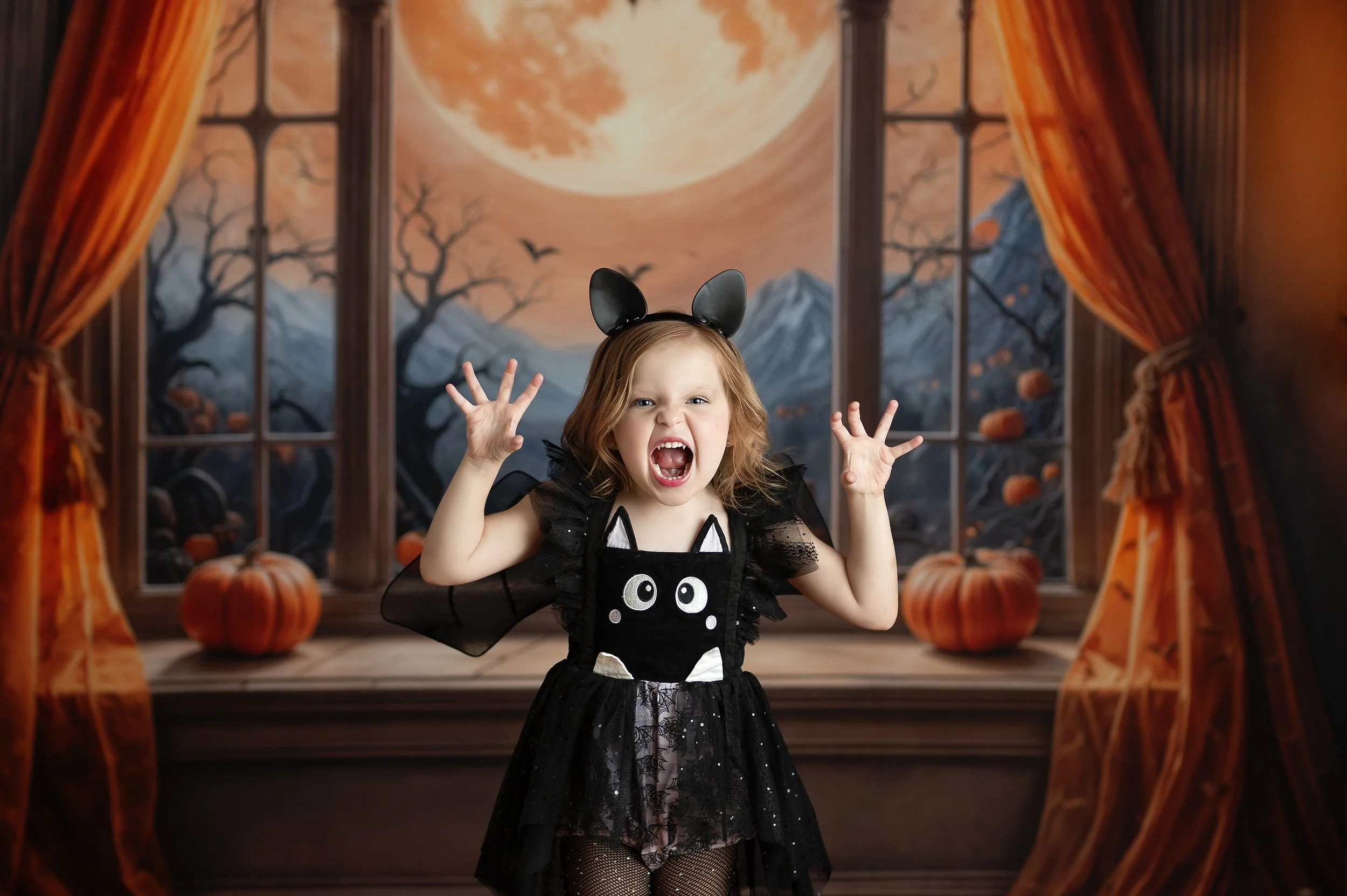 Young girl in a black Halloween costume posing in front of a warm autumn-themed backdrop.