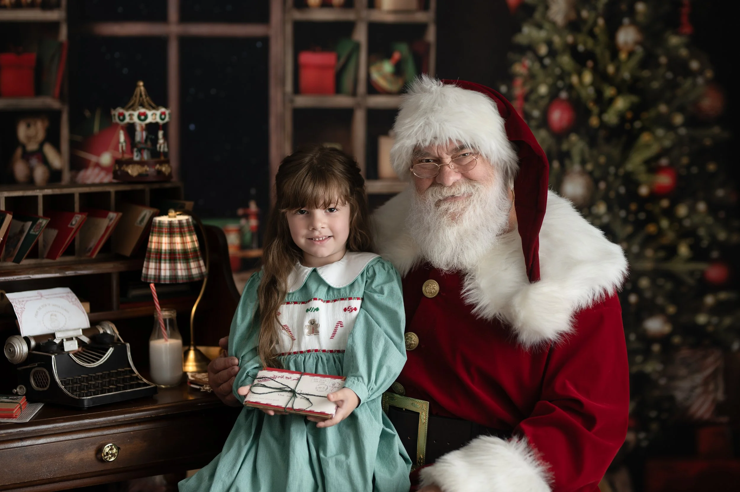 Young child sitting beside Santa during a traditional Christmas photography session.