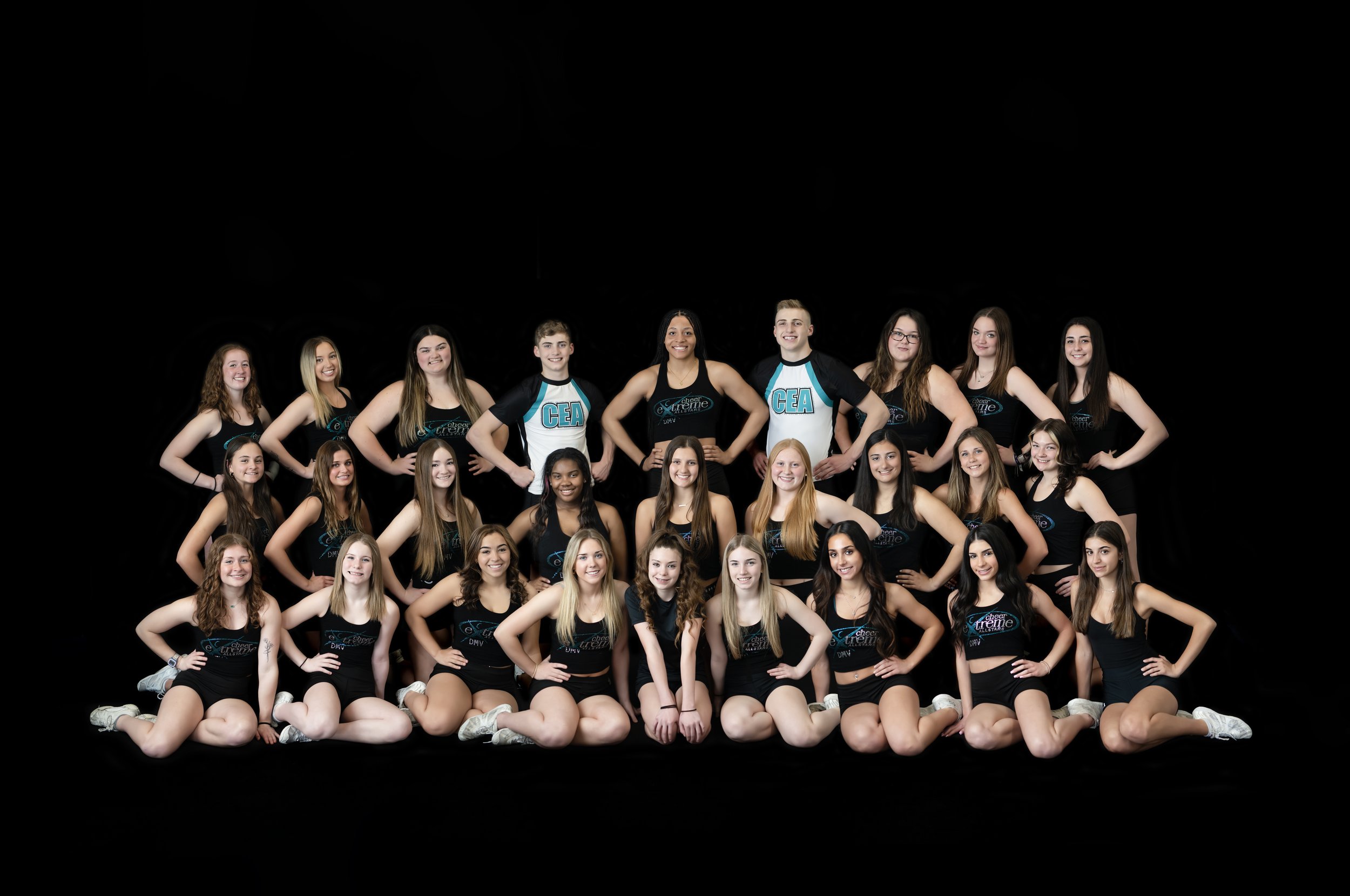Large cheer team photographed together in a studio team portrait against a black background.