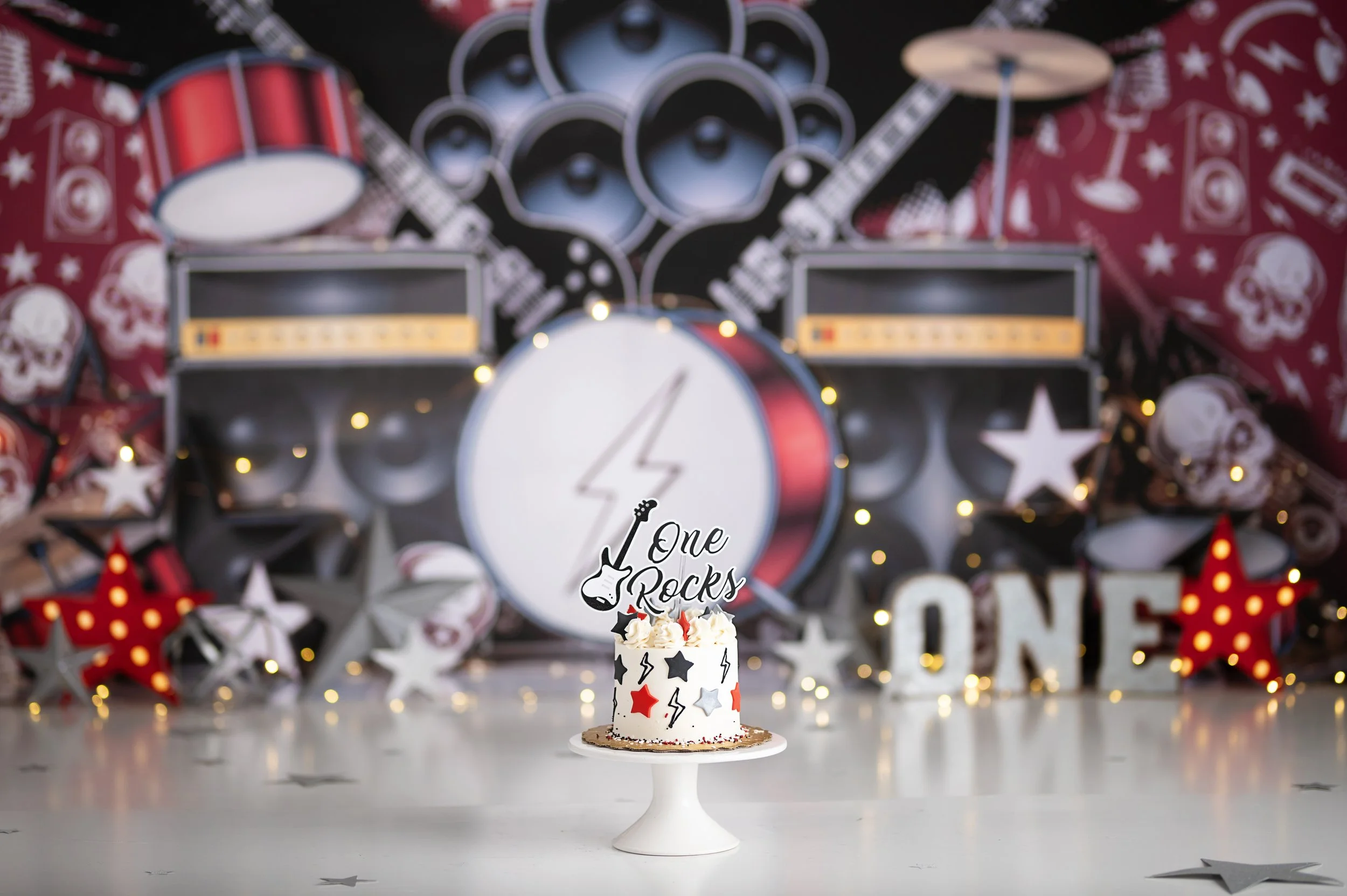 Rock music themed Cake Smash photography set featuring drums, speakers, guitars, and a first birthday cake.