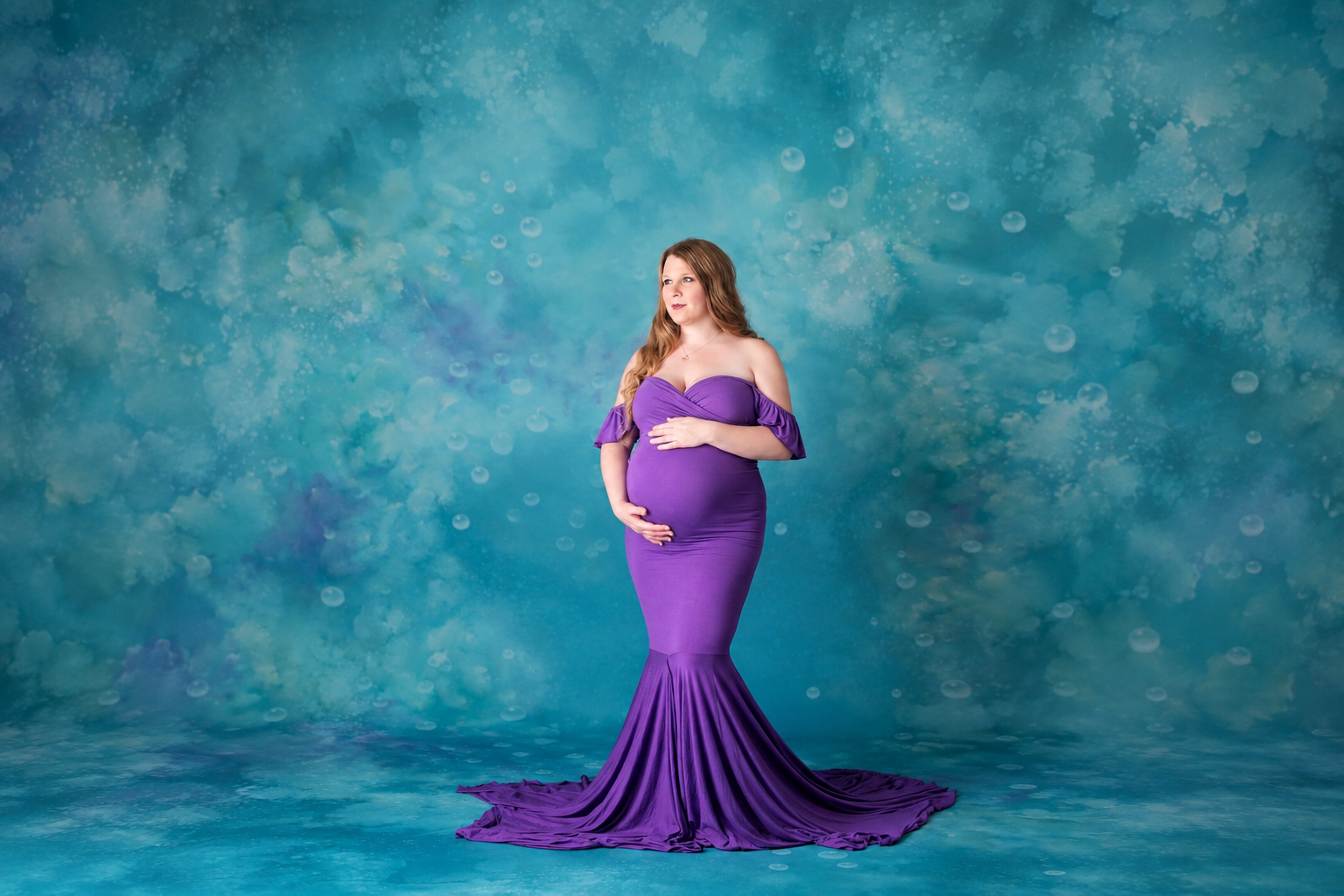 Expecting mother wearing a purple maternity gown during a studio maternity portrait session.